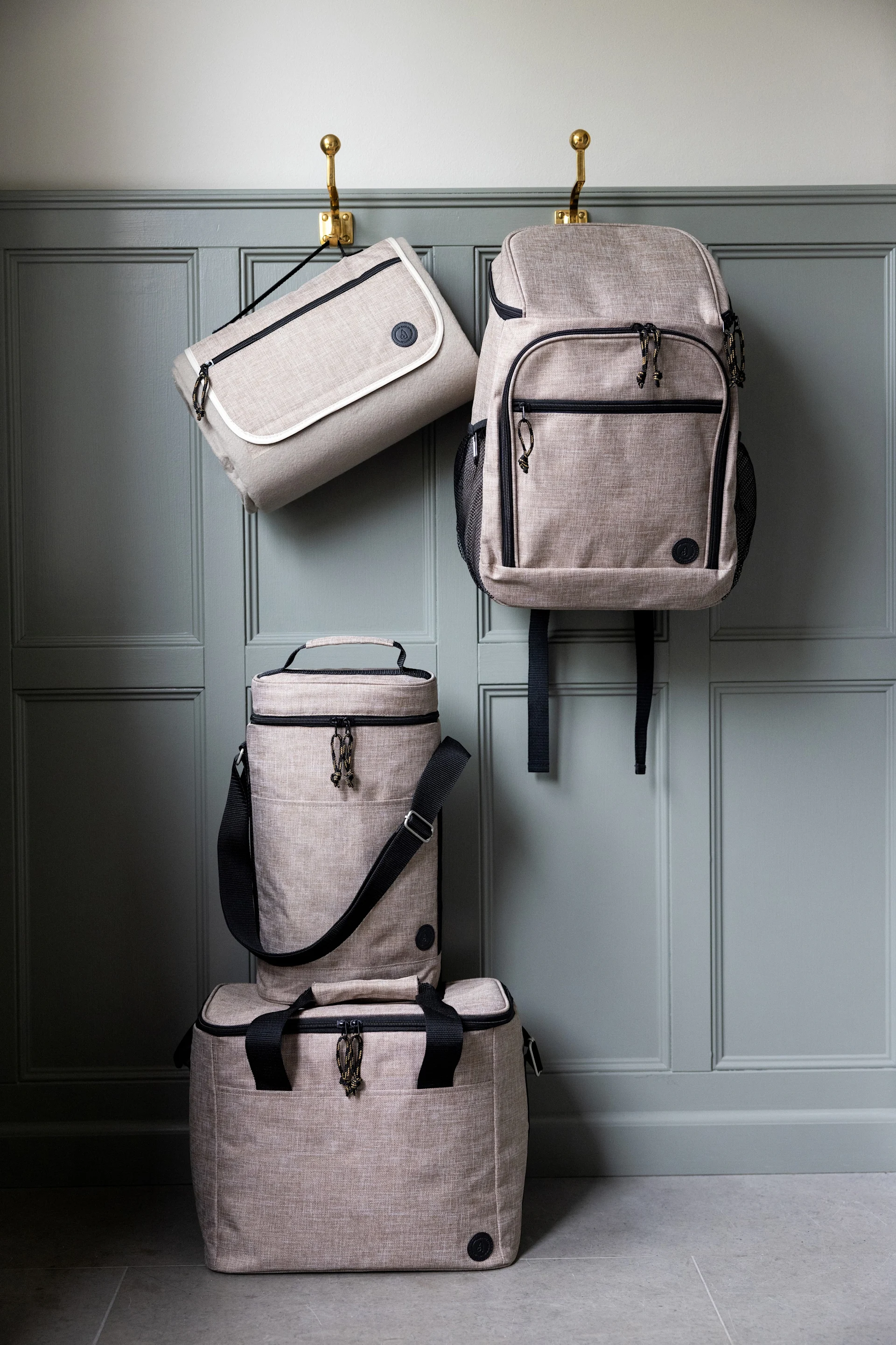 Quatre sacs de couleur beige clair : un sac plat et un sac à dos sont suspendus à des crochets, tandis qu'une glacière cylindrique et une glacière rectangulaire sont empilées en dessous.