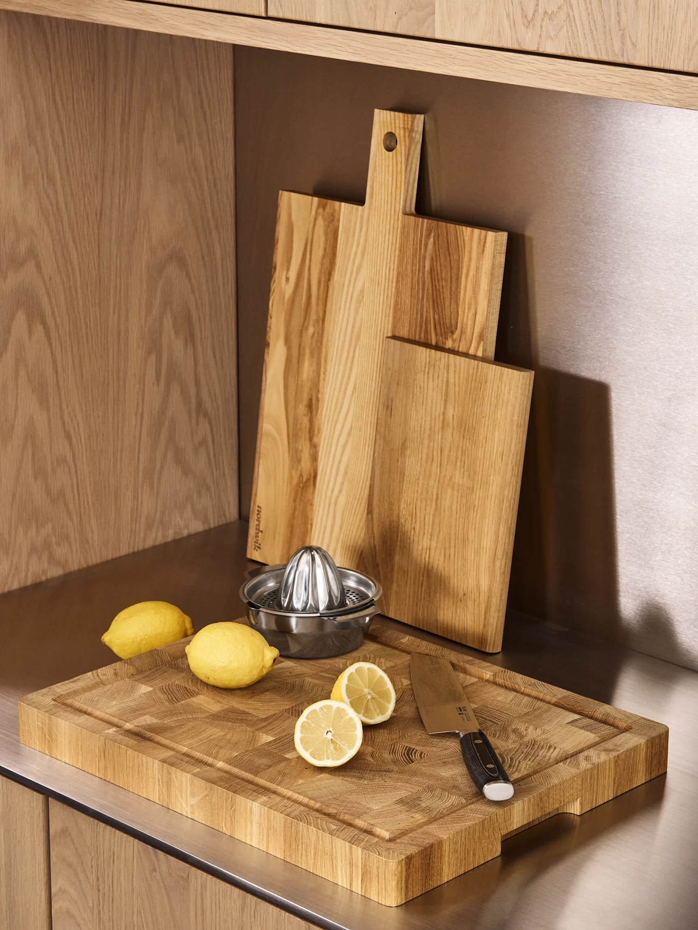 Trois planches à découper en bois, un presse-citron en acier inoxydable et des citrons frais sur un comptoir de cuisine.