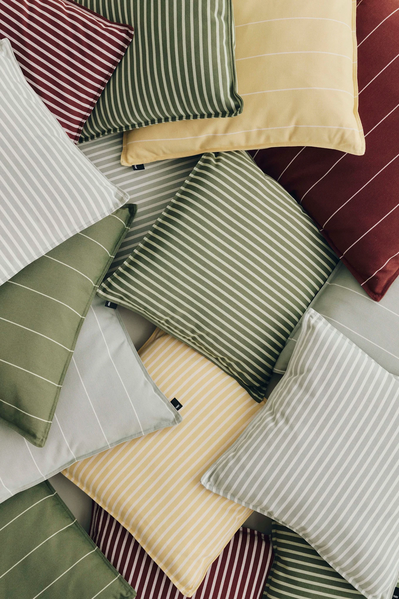 Un tas de coussins rayés en rouge, jaune, vert clair et gris clair, avec des rayures de différentes orientations.