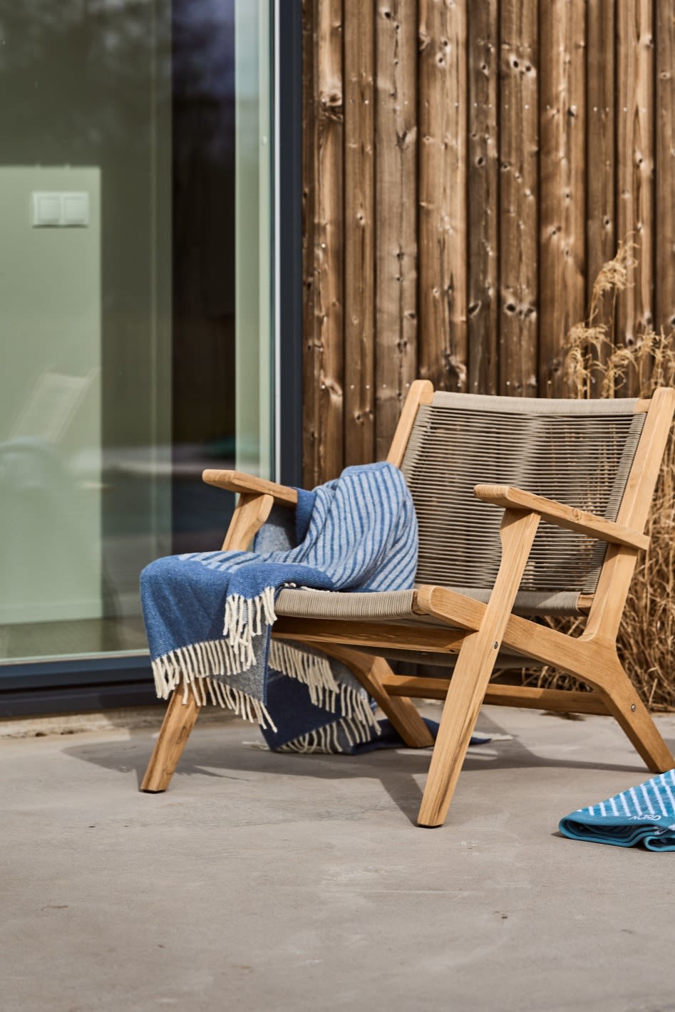 Une terrasse scandinave avec la chaise longue Sandvik de 1898 et la couverture en laine bleue Stripes de NJRD.