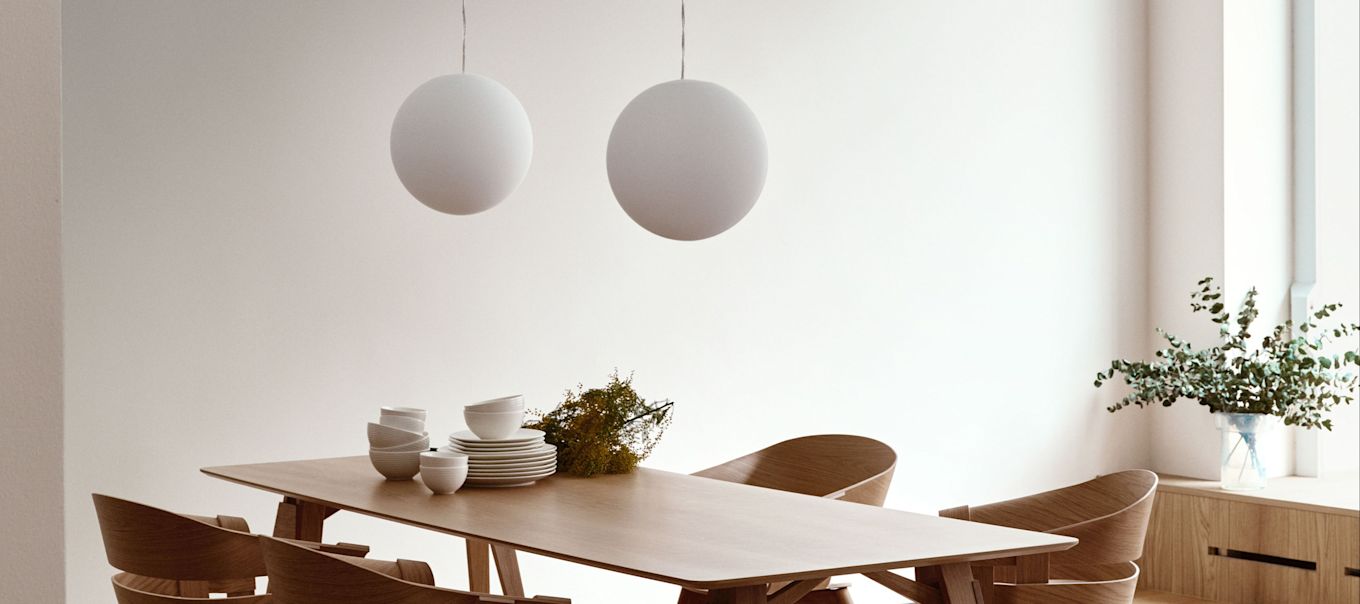 La lampe Luna de Design House Stockholm est suspendue par paire au-dessus d'une table à manger en bois. 