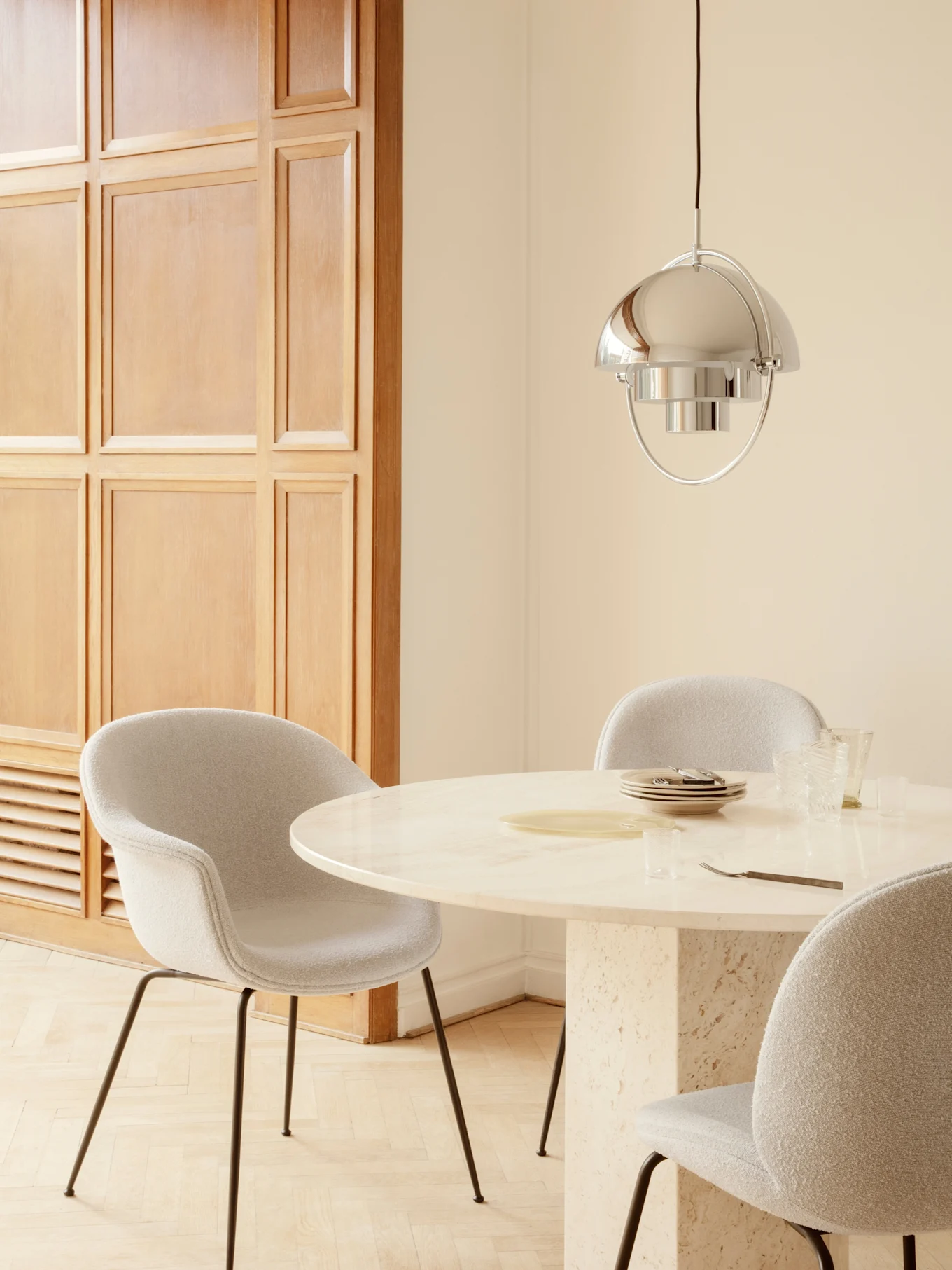 Salle à manger avec table ronde en marbre, chaises rembourrées gris clair et lampe suspendue argent polie.