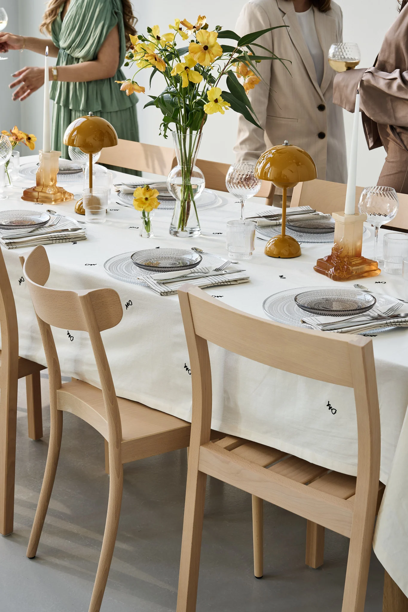 Une table de fête décorée avec des touches de jaune et des invités qui échangent autour. Ici, vous voyez la Flowerpot VP9 de Tradition accompagnée du bougeoir Rocky Baroque en ambre.