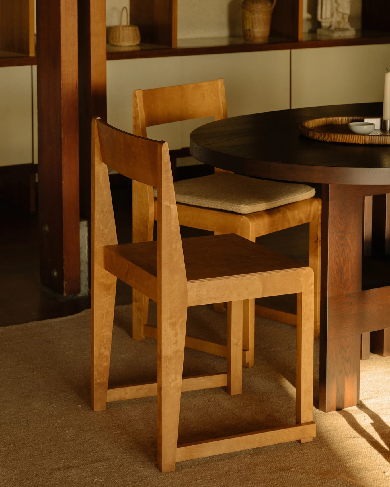 Deux chaises en bois clair autour d'une table à manger ronde foncée, avec des étagères en bois en arrière-plan.