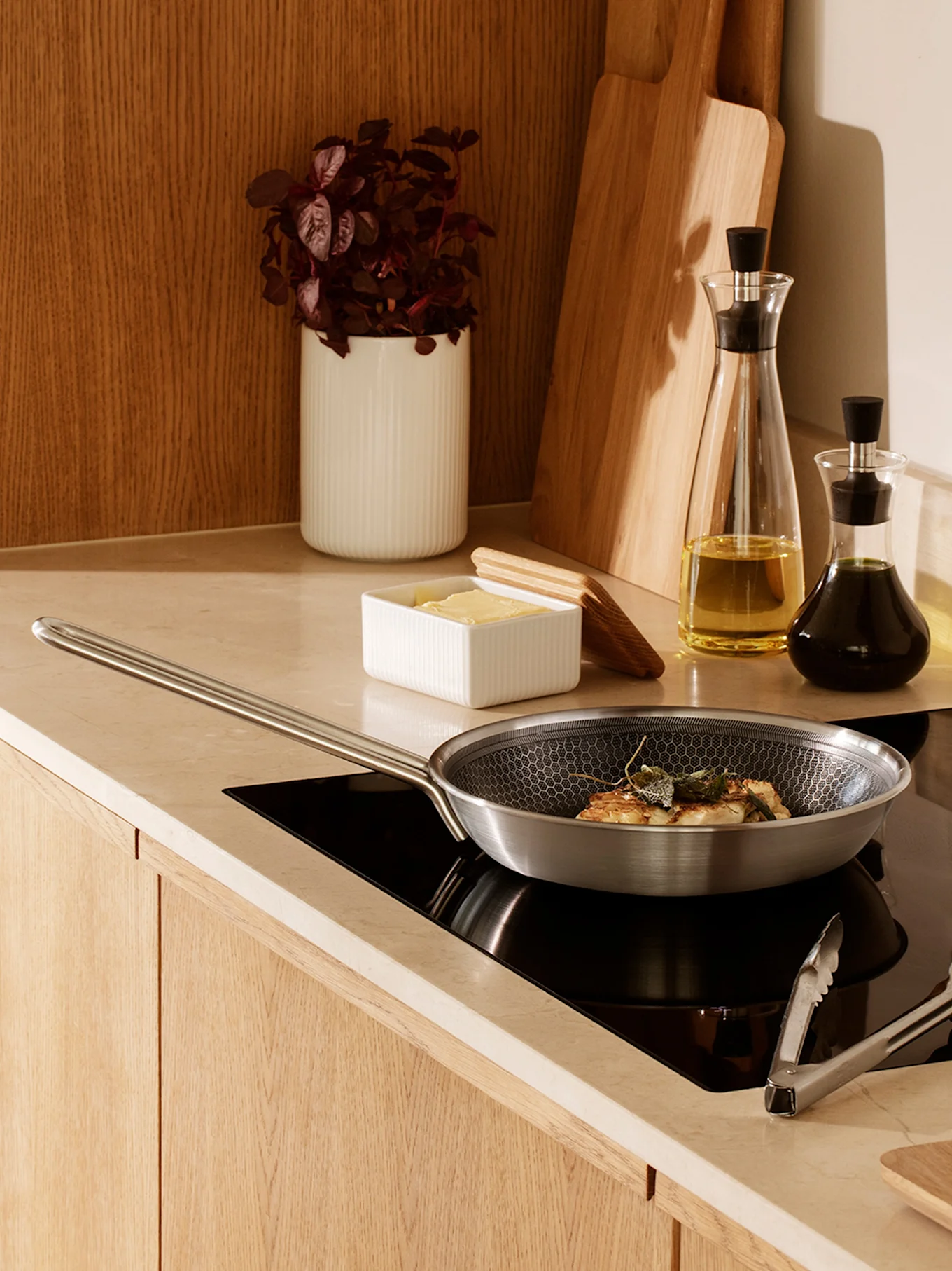 Une poêle en acier inoxydable avec motif nid d'abeille cuisinant des aliments avec de la sauge sur une plaque à induction noire dans une cuisine moderne.