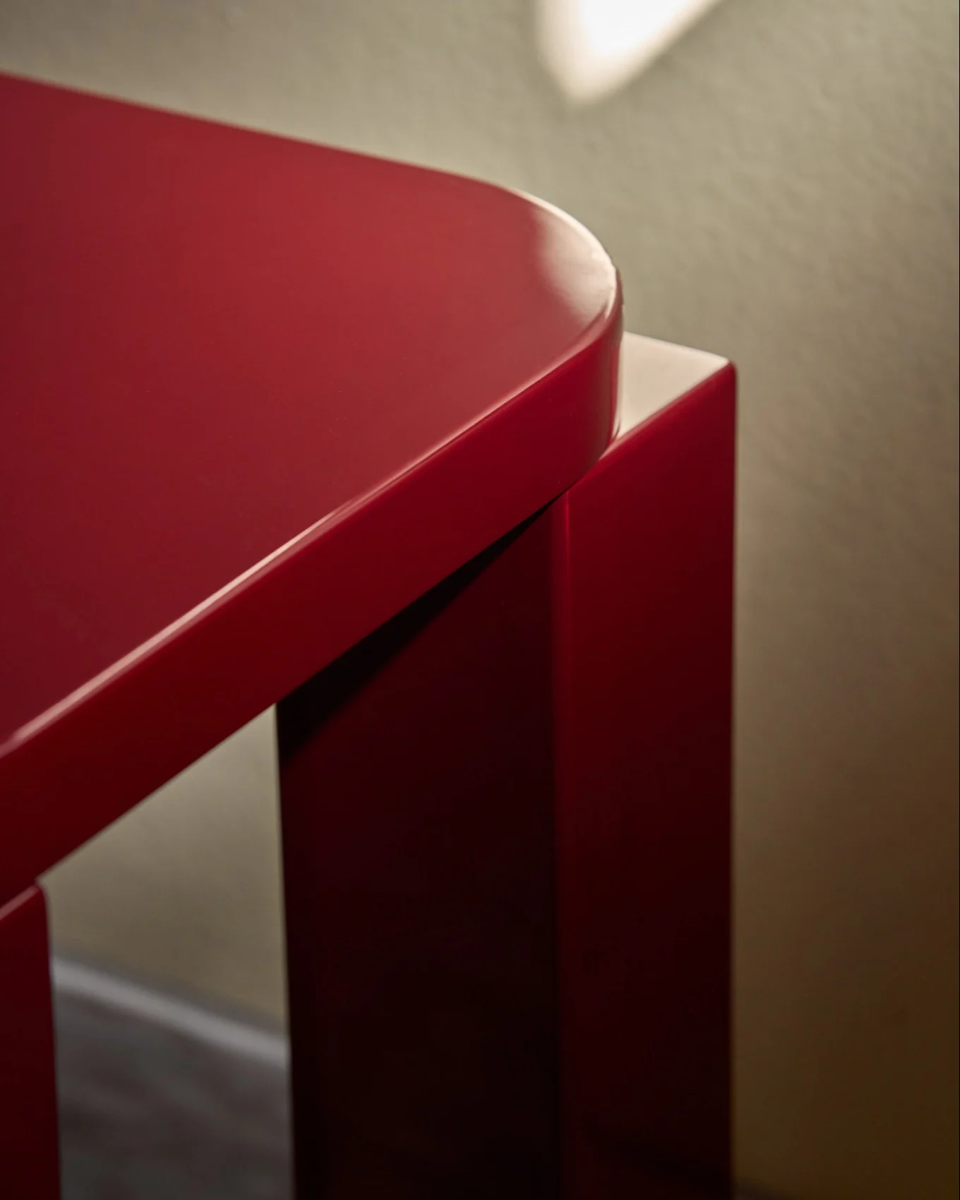 Un tabouret rouge brillant avec un plateau rectangulaire arrondi, sur un sol carrelé à côté d'un mur aux carreaux rouges.