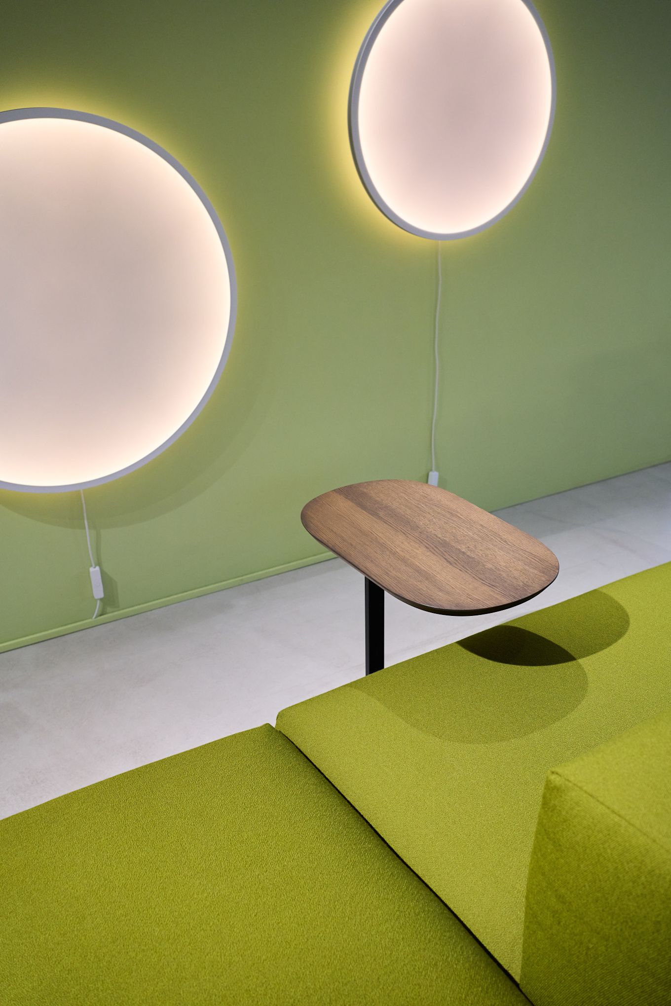 Une pièce avec un mur vert sur lequel sont suspendues deux appliques rondes Calm, devant lequel se trouve un canapé vert avec une table d'appoint Relate.