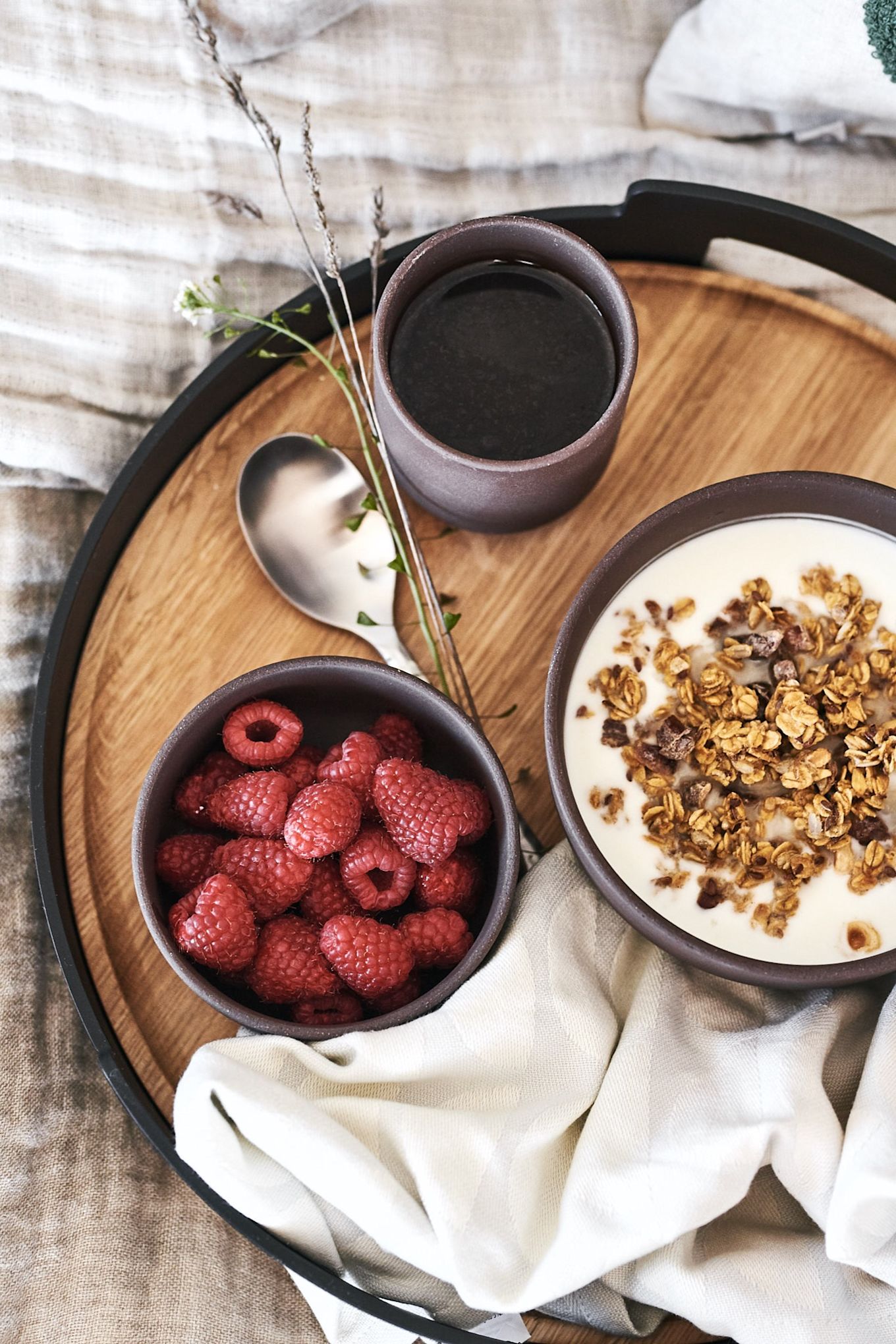 Un petit-déjeuner de luxe au lit servi sur un magnifique plateau d'Eva Solo avec des baies et du muesli dans des bols bruns de Ferm Living.