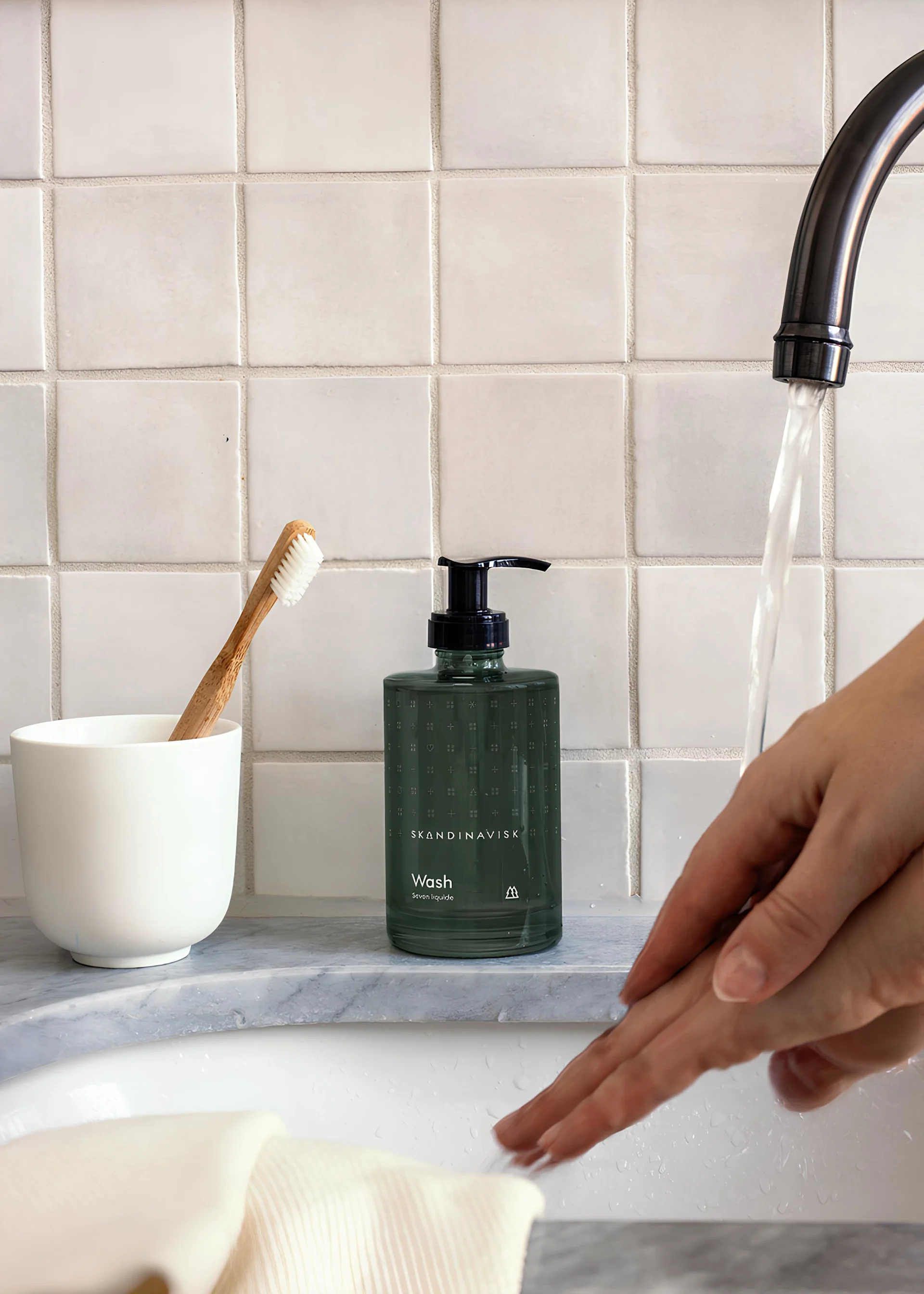 Cadeau pour la Saint-Valentin : offrez des moments de détente. Ici, le savon Skog de Skandinavisk est posé sur un lavabo tandis qu'une personne se lave les mains.