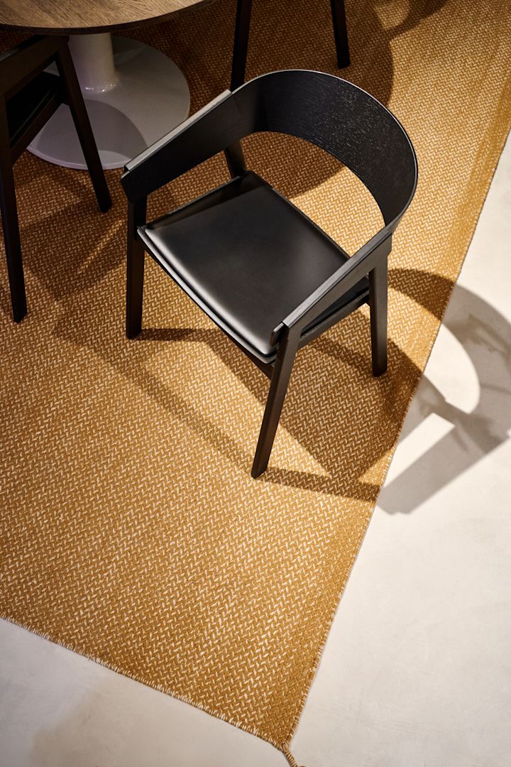 Le fauteuil Cover noir avec assise en cuir de Muuto est posé sur un tapis couleur moutarde.