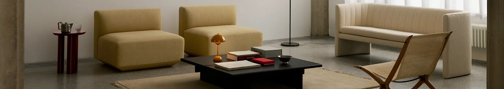 Un salon moderne avec deux fauteuils moutarde sans accoudoirs, une table basse noire, un canapé côtelé crème et une chaise en bois tressé.