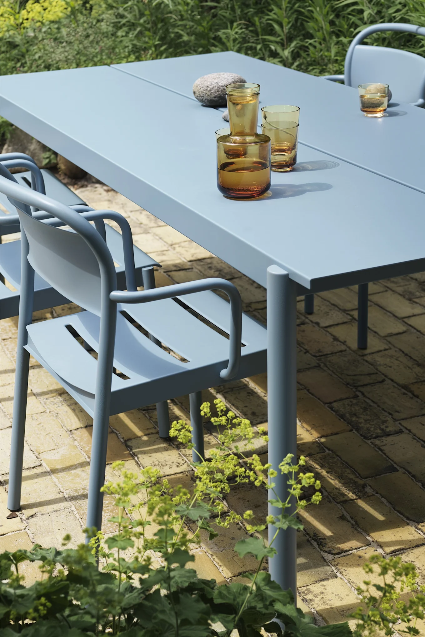 La chaise de la collection Linear en Pale Blue de Muuto se trouve ici à côté de la table correspondante et séduit par sa forme douce et arrondie. Elle est donc tout à fait dans la tendance en matière de meubles de jardin en 2025.
