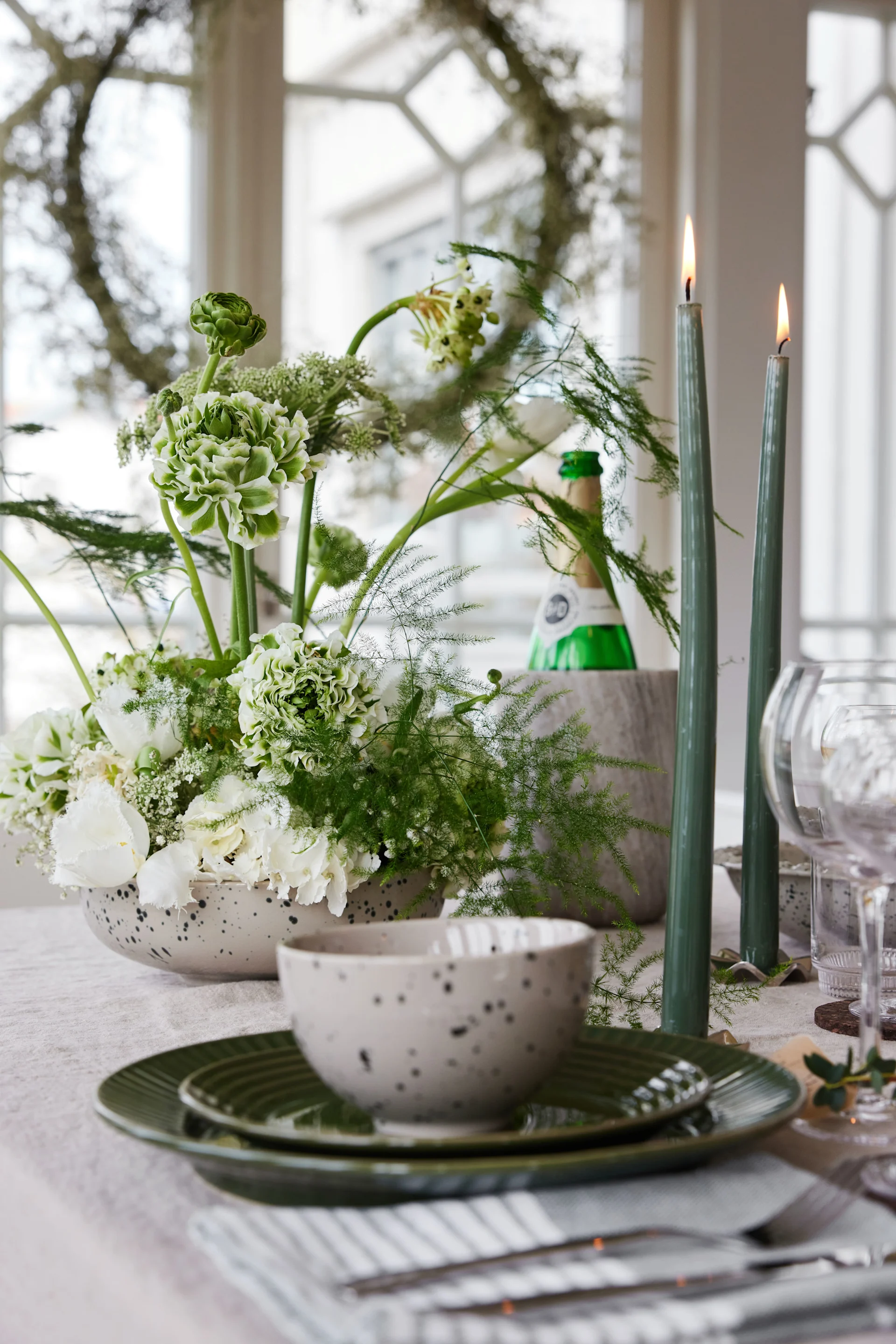 Une table dressée avec des assiettes, des fleurs, des bougies et un seau à vin.