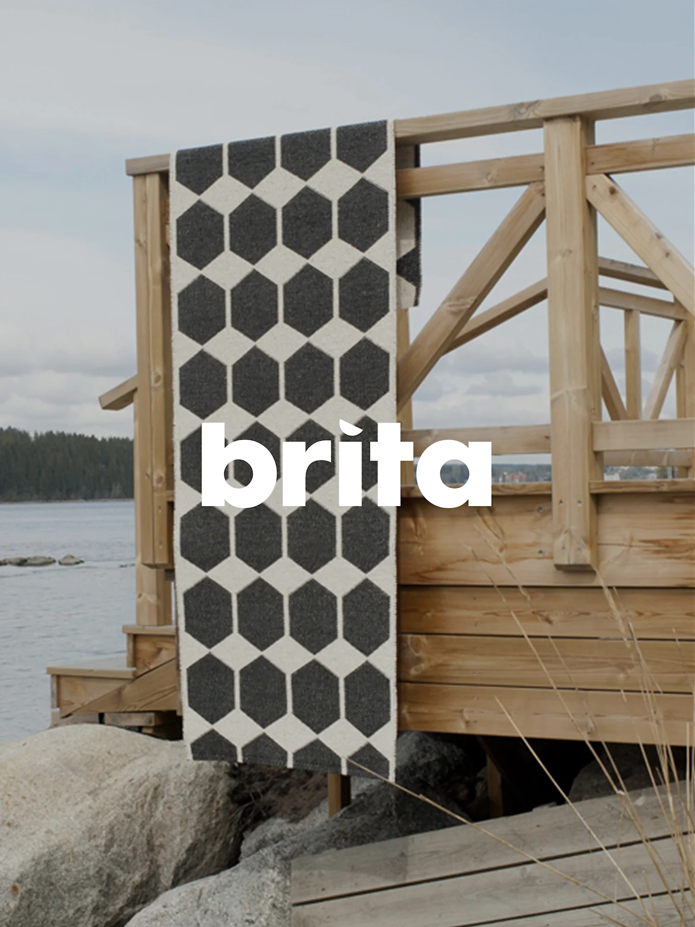 Un tapis de couloir hexagonal noir et blanc, drapé sur une balustrade en bois près de l'eau et des rochers.