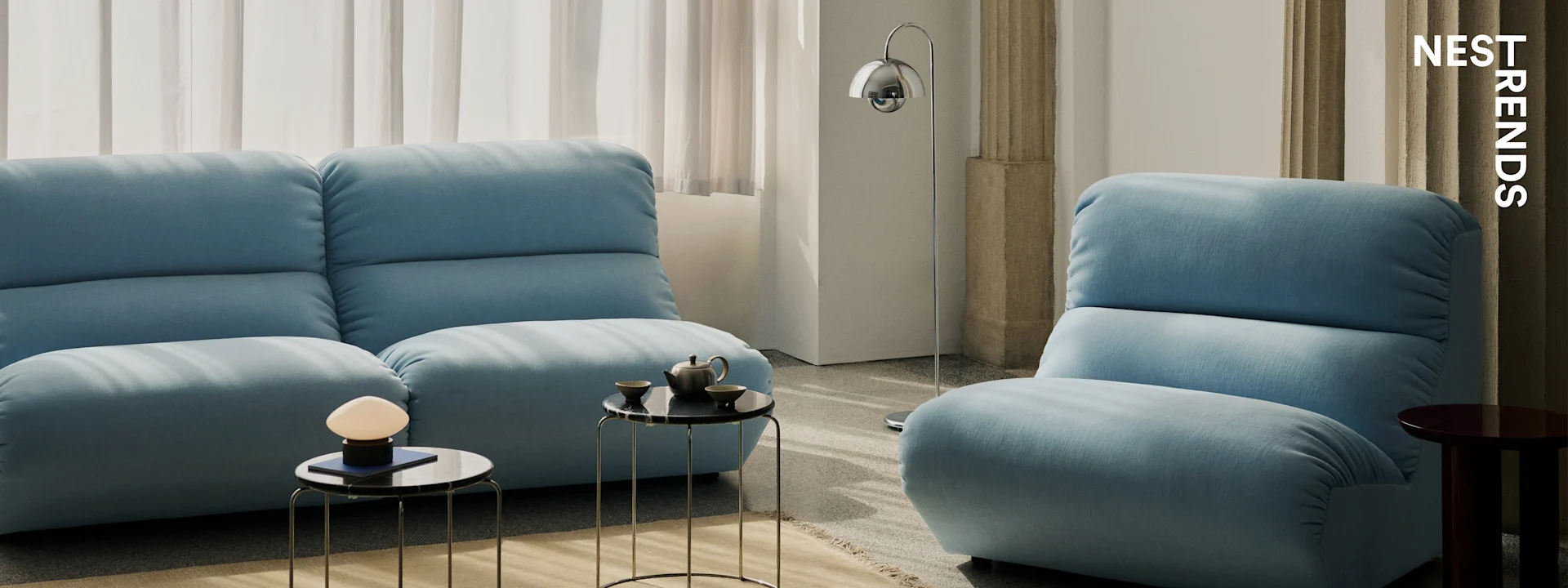 Salon moderne avec deux canapés bleu clair, des tables d'appoint en marbre noir et des lampes élégantes.