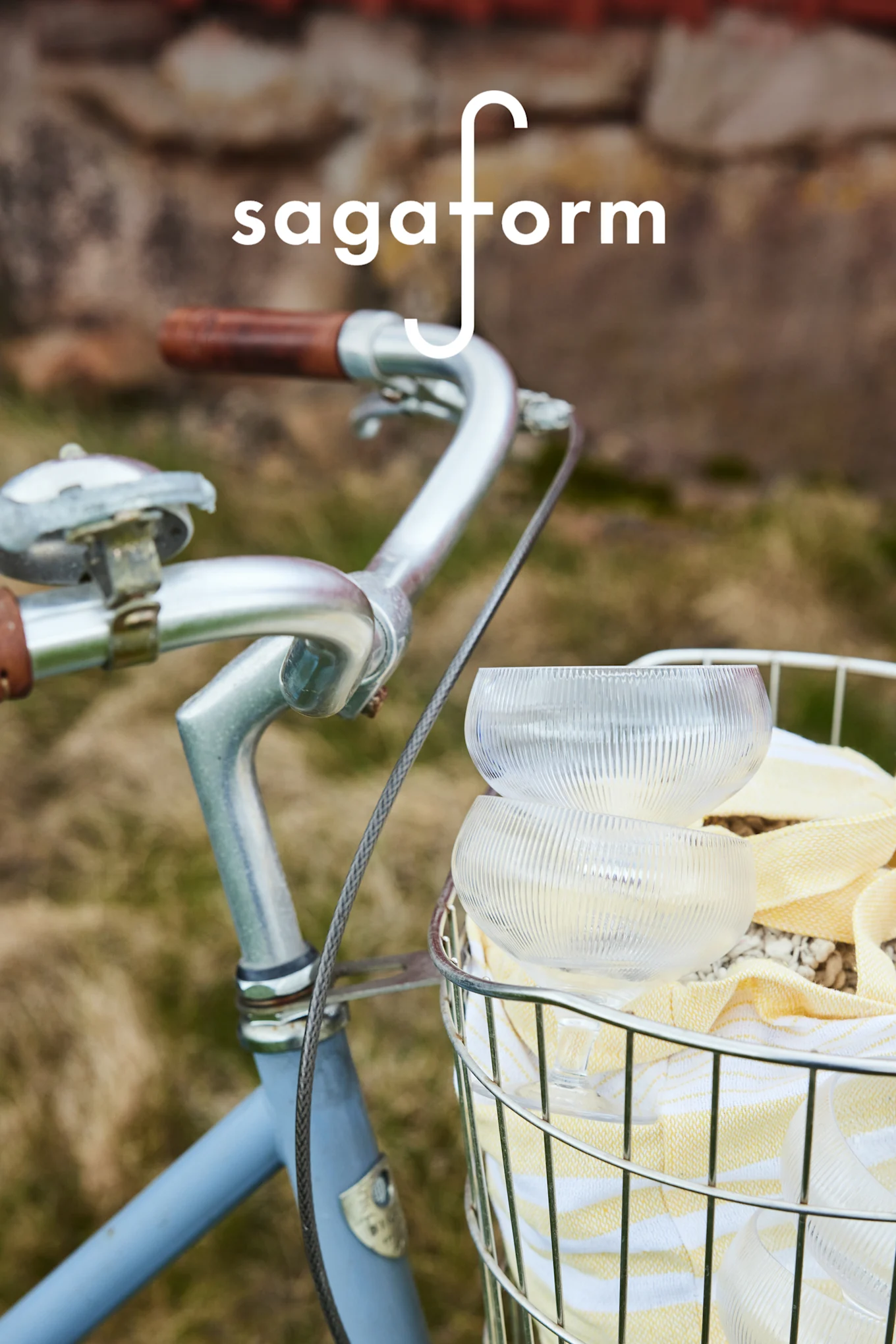 Deux bols en verre transparents et nervurés et une serviette à rayures jaunes dans un panier de vélo. Logo 'sagaform'.