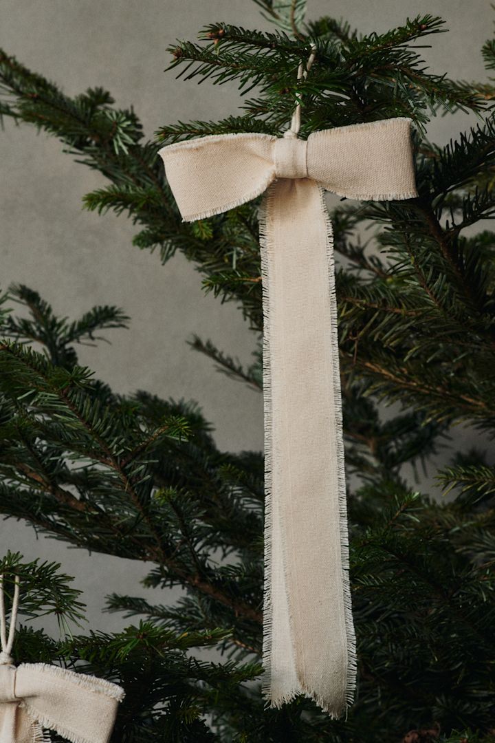 Une décoration en forme d'arc de Ferm Living est suspendue à un sapin de Noël.