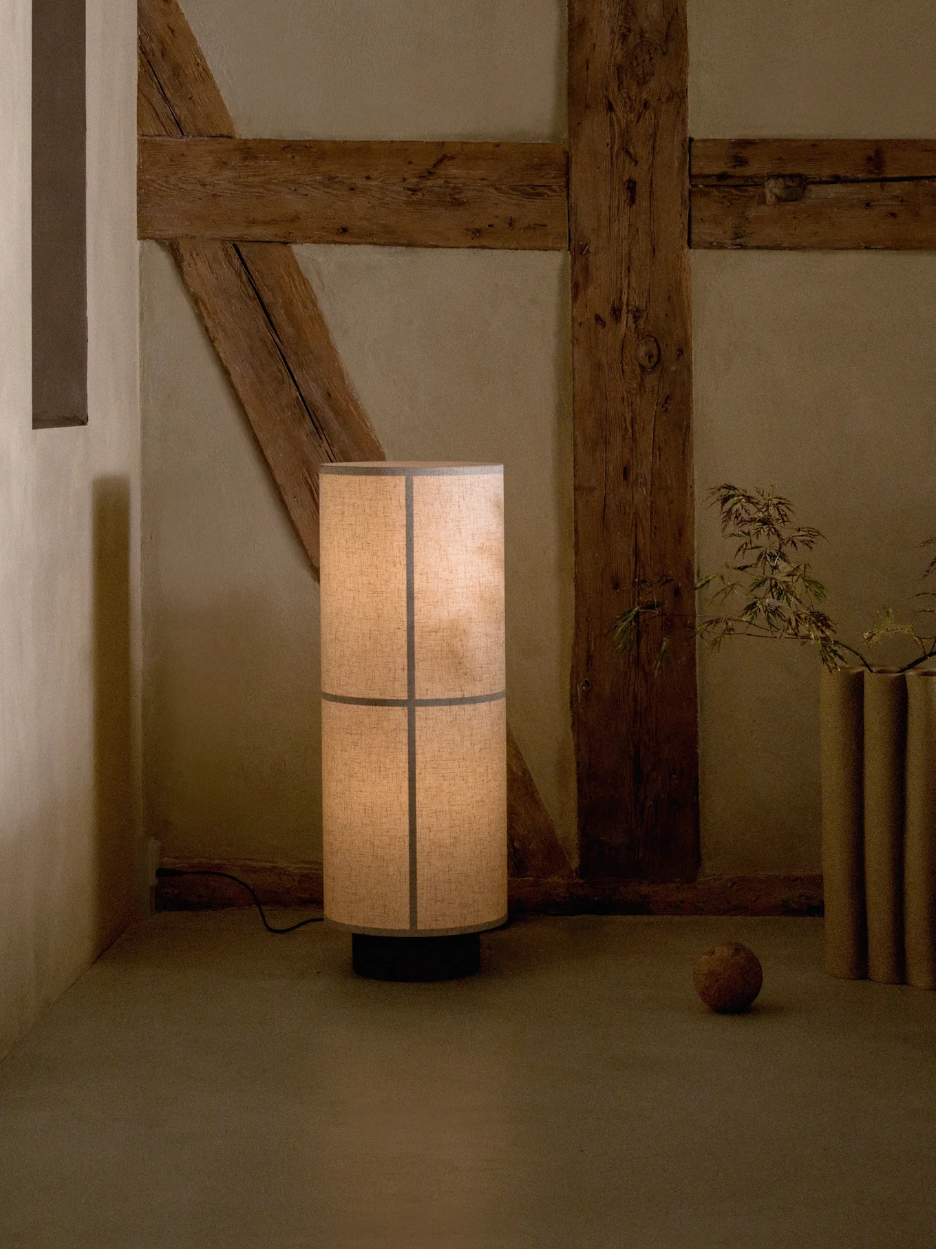 Grand lampadaire avec un abat-jour en tissu segmenté, projetant une lueur chaleureuse dans une pièce rustique avec des poutres en bois apparentes.