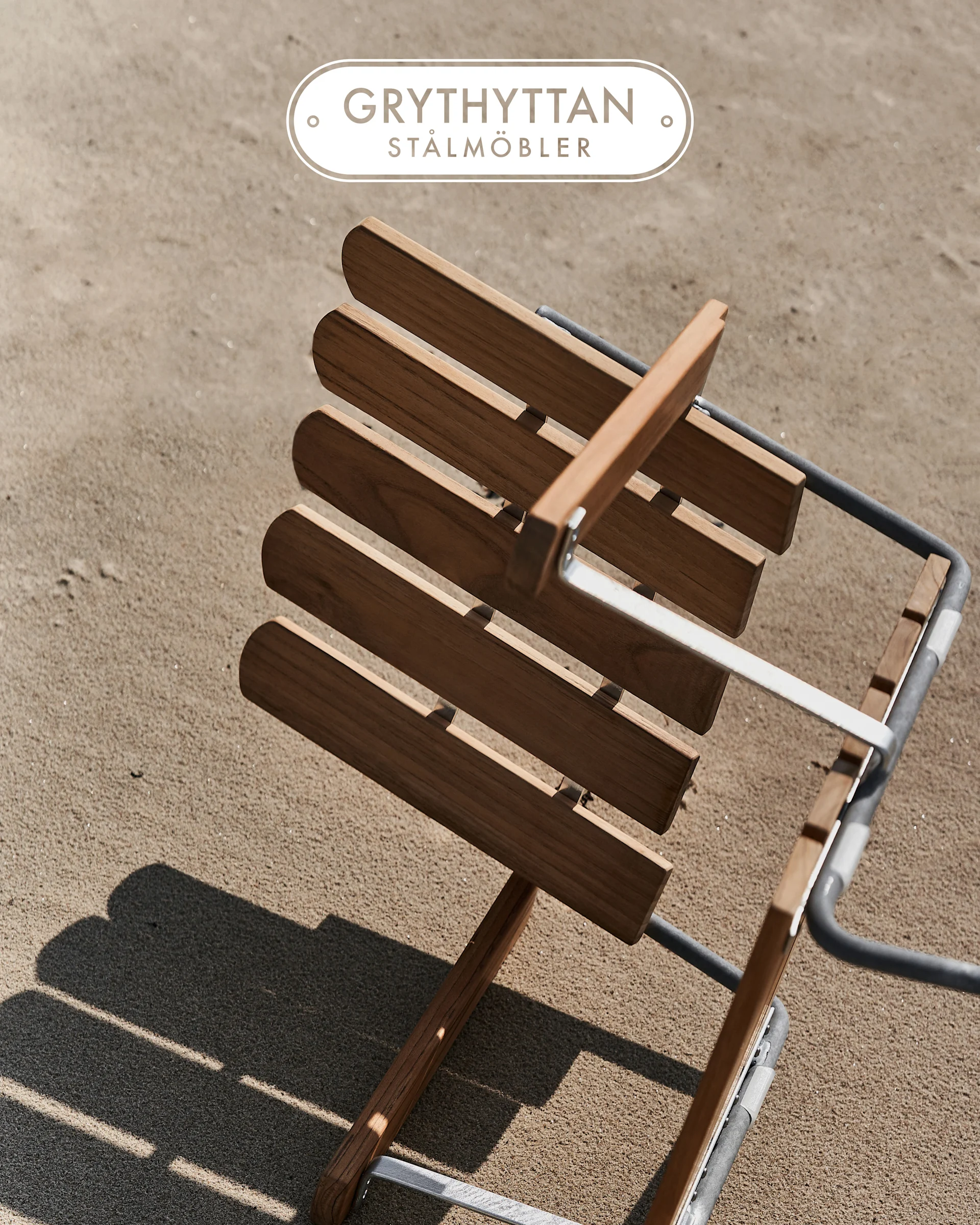 Chaise à lattes en bois avec cadre métallique sur le sable, vue d'en haut. Logo Grythyttan Stålmöbler.
