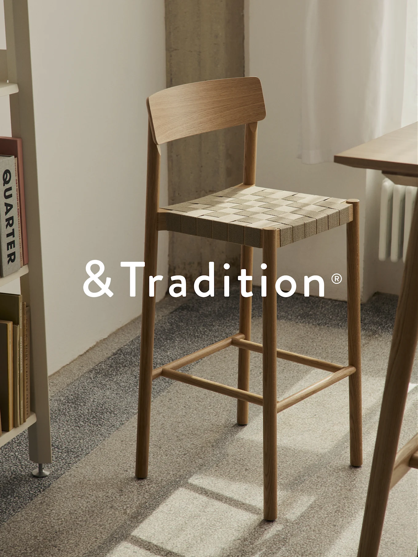 Haut tabouret de bar en bois clair avec assise tressée, sur un sol texturé.