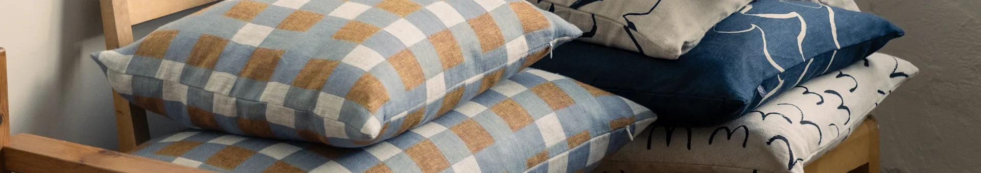 Coussins empilés sur une chaise en bois, présentant des motifs à carreaux bleus et bruns, et des motifs abstraits bleus et beiges.