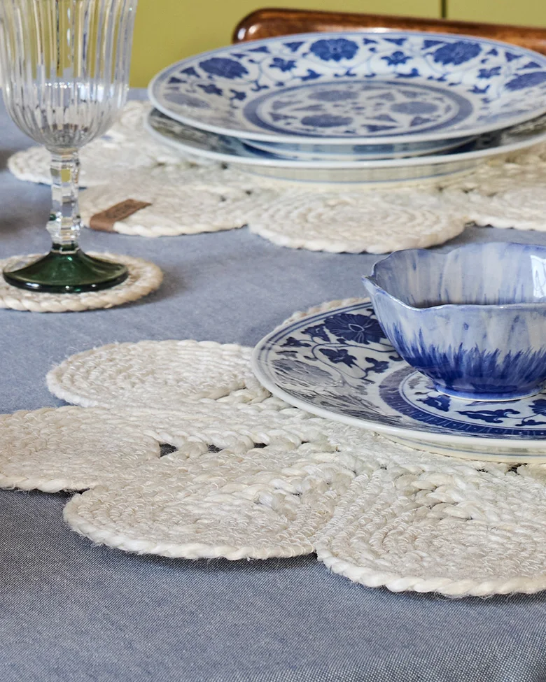 Table dressée avec vaisselle bleue et blanche, sets de table floraux tressés blancs et un verre nervuré.