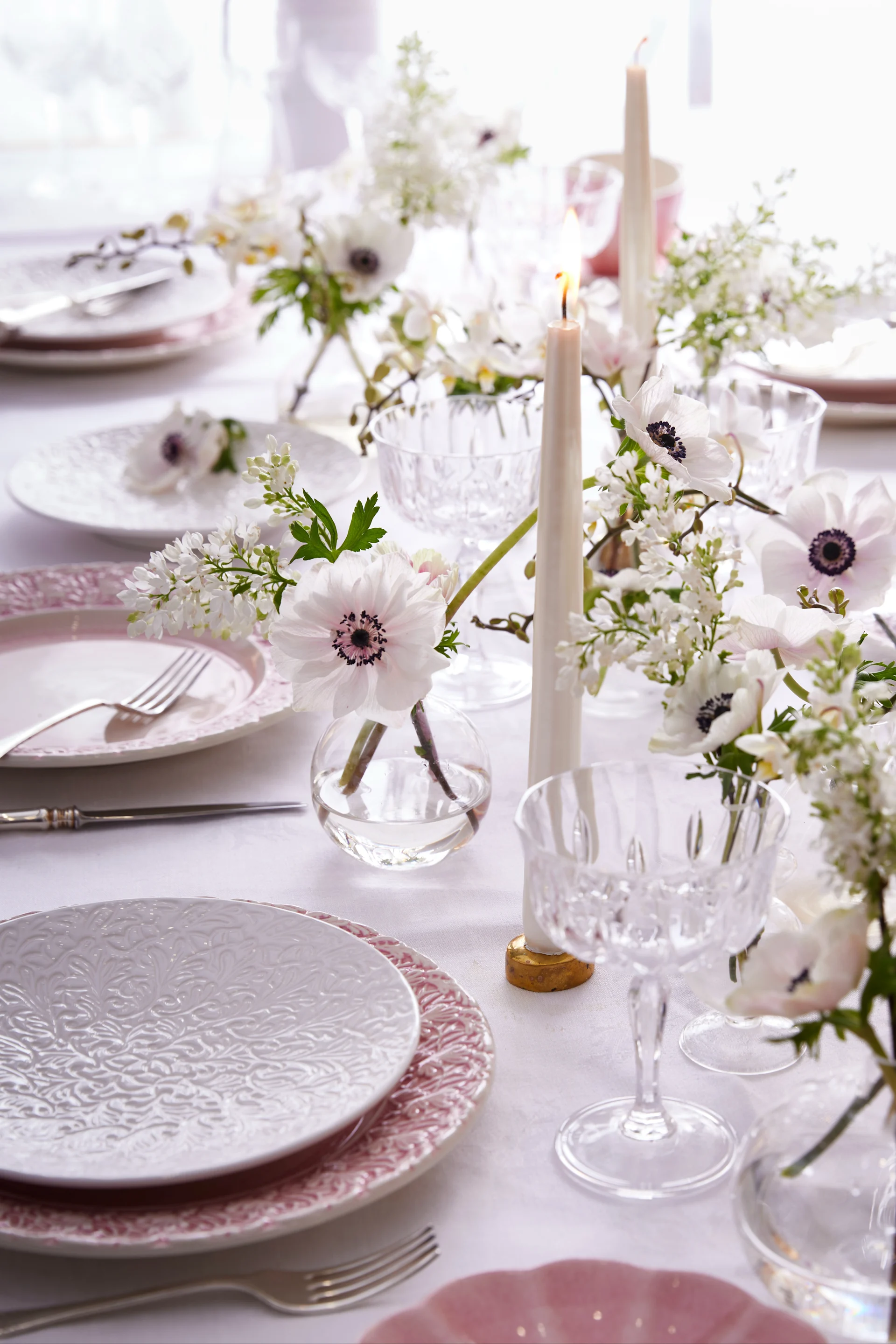 Décorations de table en blanc et rose, assiettes de la collection Lace de Mateus, verres élégants, bougies et fleurs.