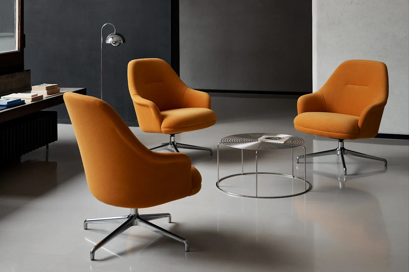 Trois fauteuils pivotants orange disposés autour d'une table basse ronde chromée dans une pièce moderne.