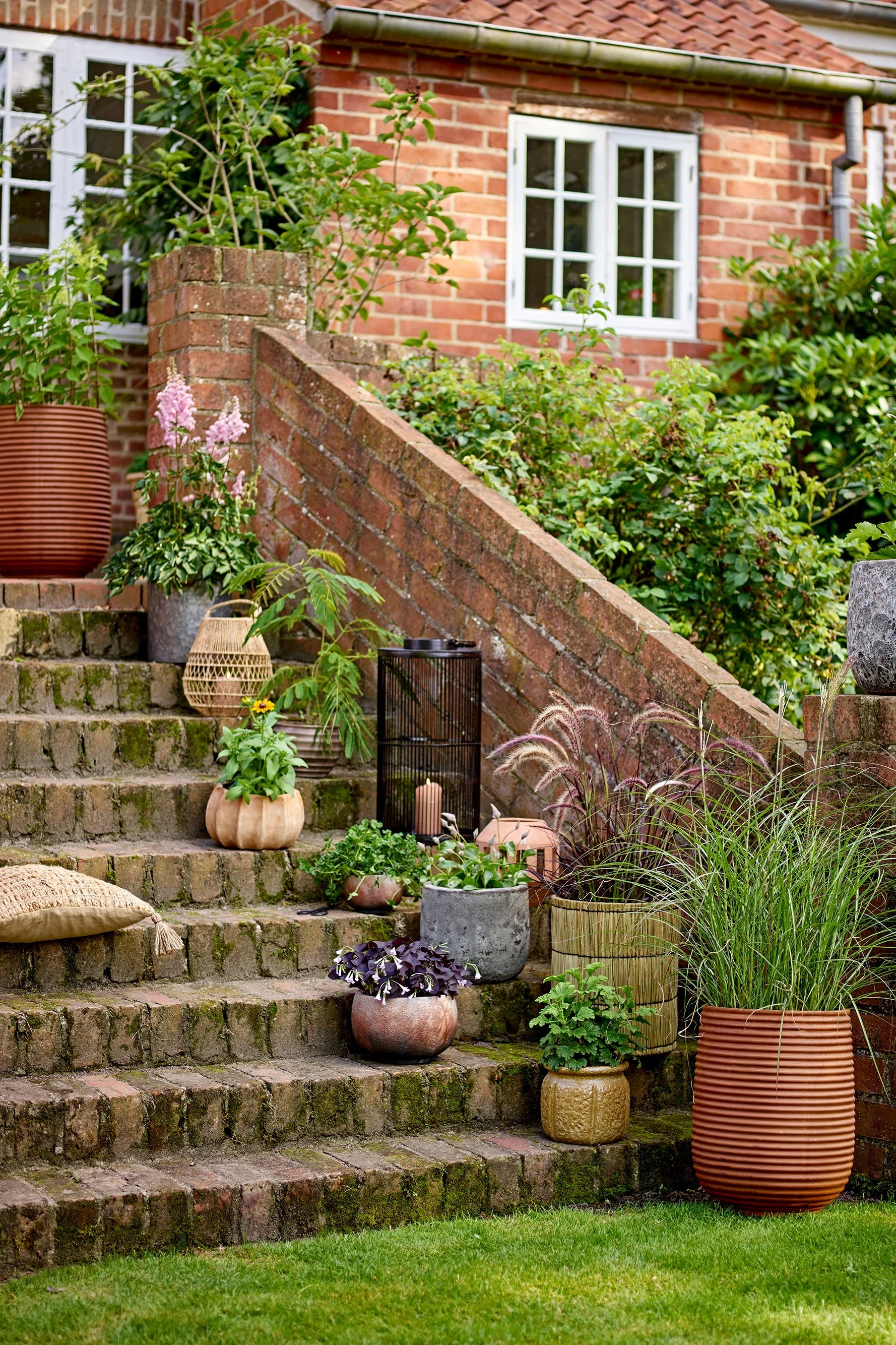 Sur un escalier dans le jardin, divers pots de fleurs de style bohème contenant des plantes sont disposés, dont le pot de fleurs Mesola de Bloomingville.