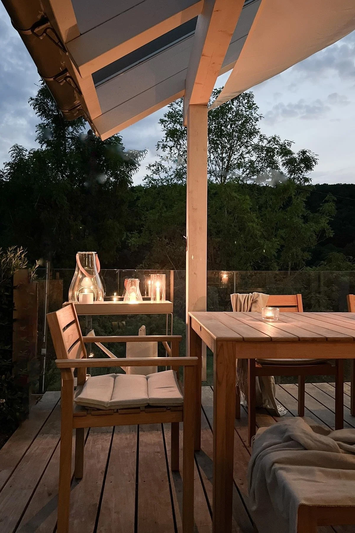 Placez plusieurs lanternes et photophores sur votre terrasse pour créer une ambiance chaleureuse. Ici, vous voyez la lanterne Design with Light de Holmegaard posée sur la table de terrasse en bois de l'influenceuse allemande @zuhauselig.