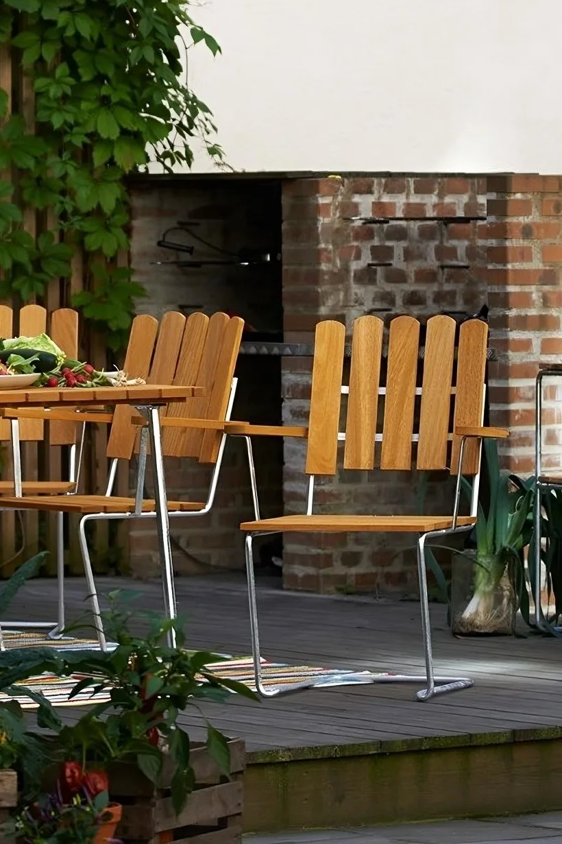 La chaise A2 de Grythyttan est en teck et en acier, visible ici sur une terrasse, et s'inscrit donc parfaitement dans les tendances 2025 en matière de mobilier de jardin.