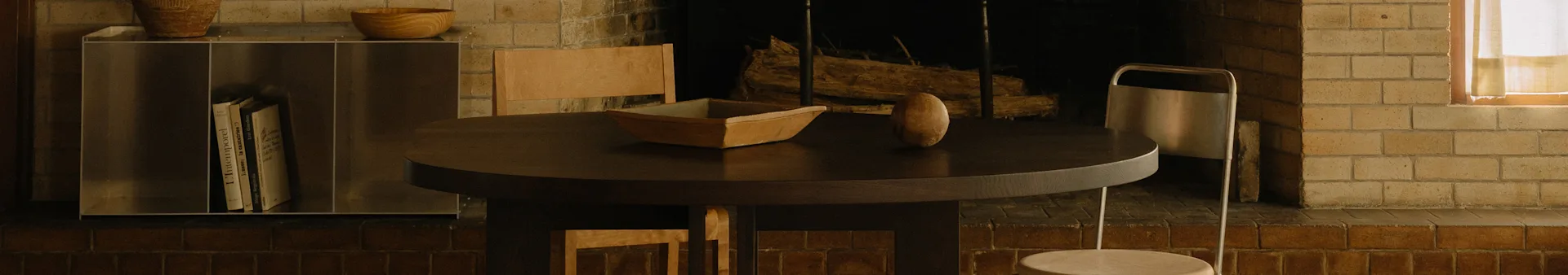 Un espace repas confortable avec une table ronde en bois foncé, un bol en bois, un objet ovale, des chaises et une cheminée.
