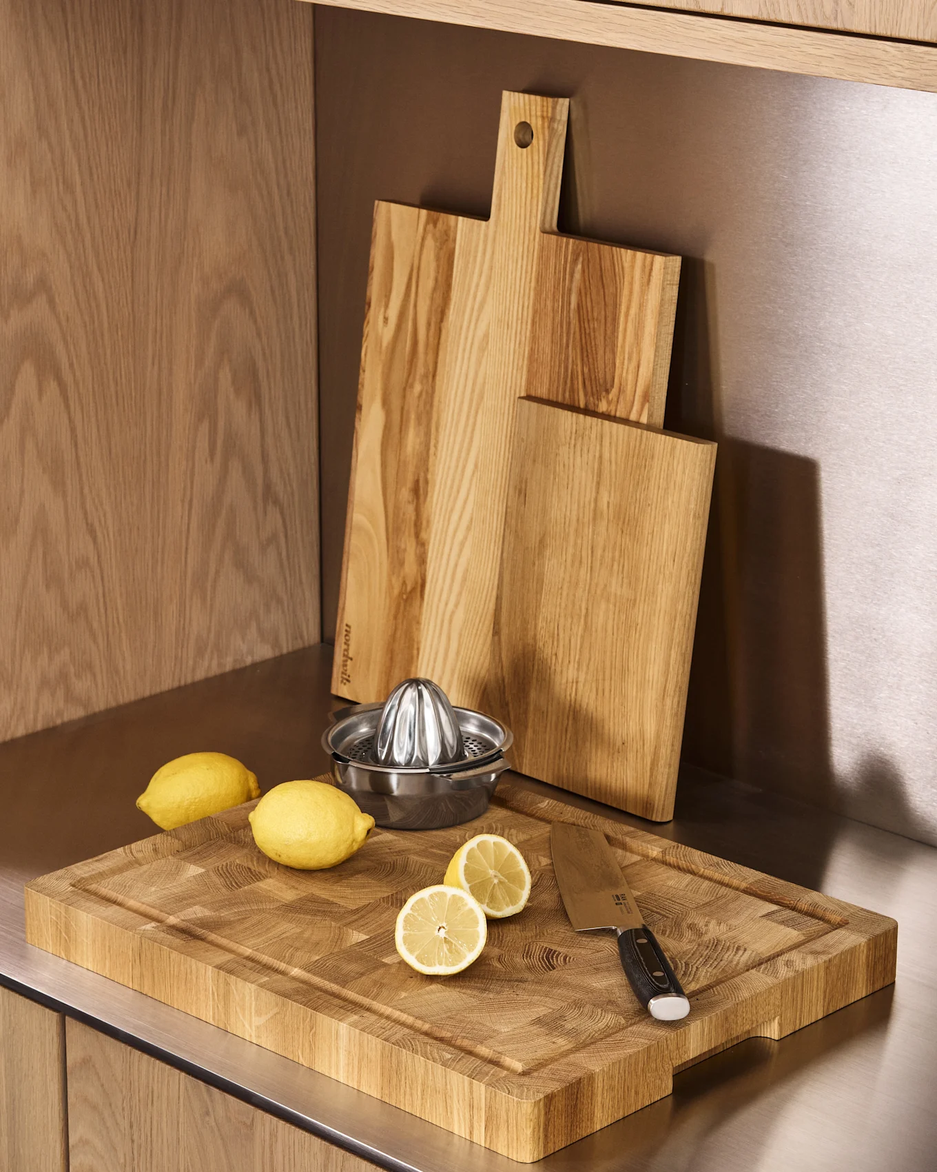Comptoir de cuisine avec trois planches à découper en bois, un presse-citron métallique, des citrons entiers et coupés, et un couteau.