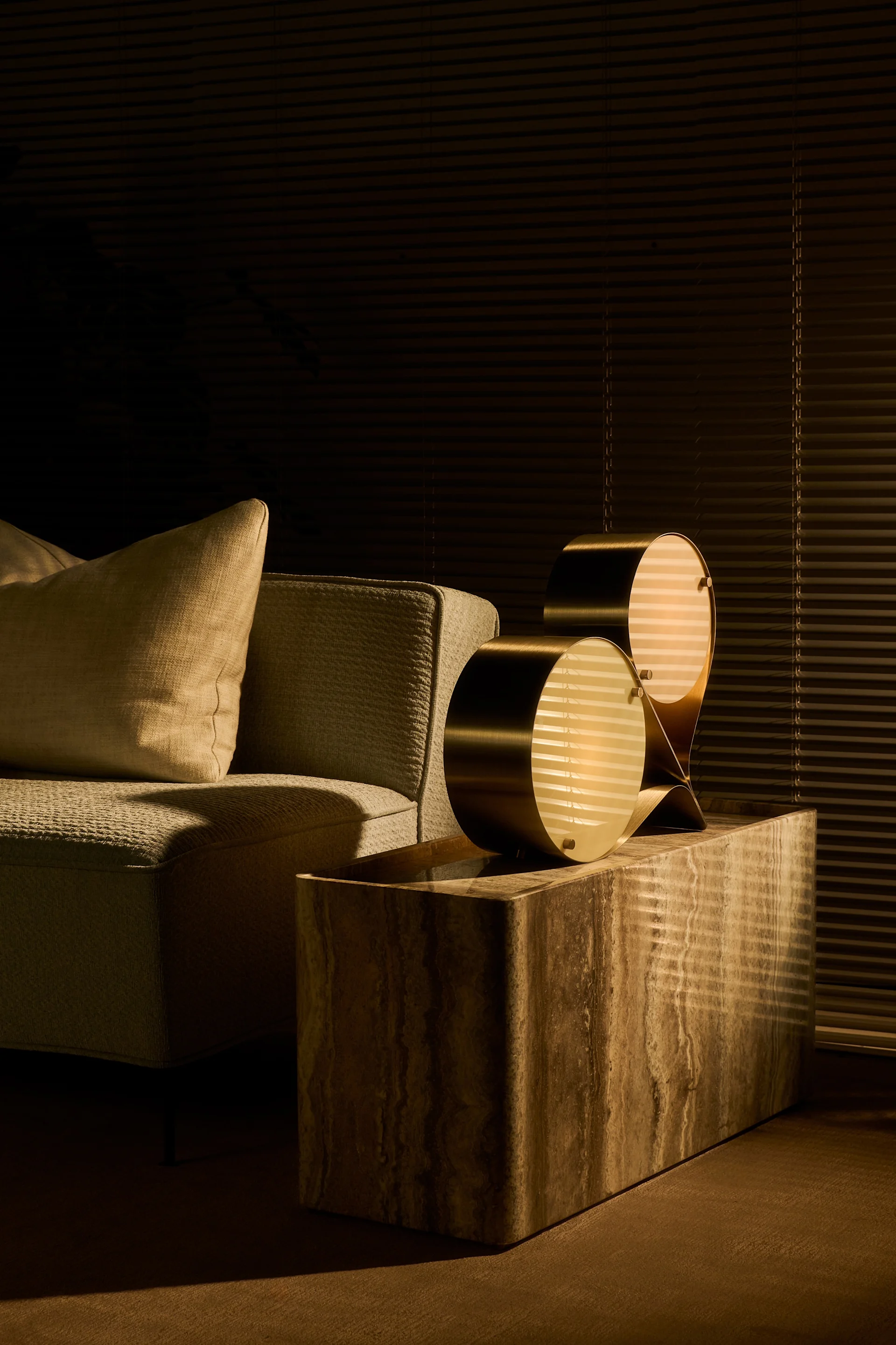 Les couleurs naturelles et la pierre font partie des tendances de la décoration d'intérieur de l'automne 2025. Ici, la lampe Coppia est posée sur la table d'appoint Pietra, toutes deux de Gubi, dans un salon.