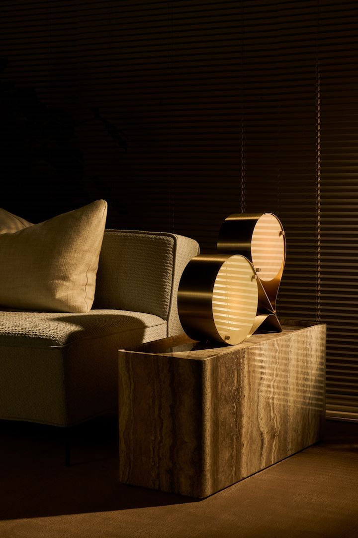 Les couleurs naturelles et la pierre font partie des tendances de la décoration d'intérieur de l'automne 2025. Ici, la lampe Coppia est posée sur la table d'appoint Pietra, toutes deux de Gubi, dans un salon.