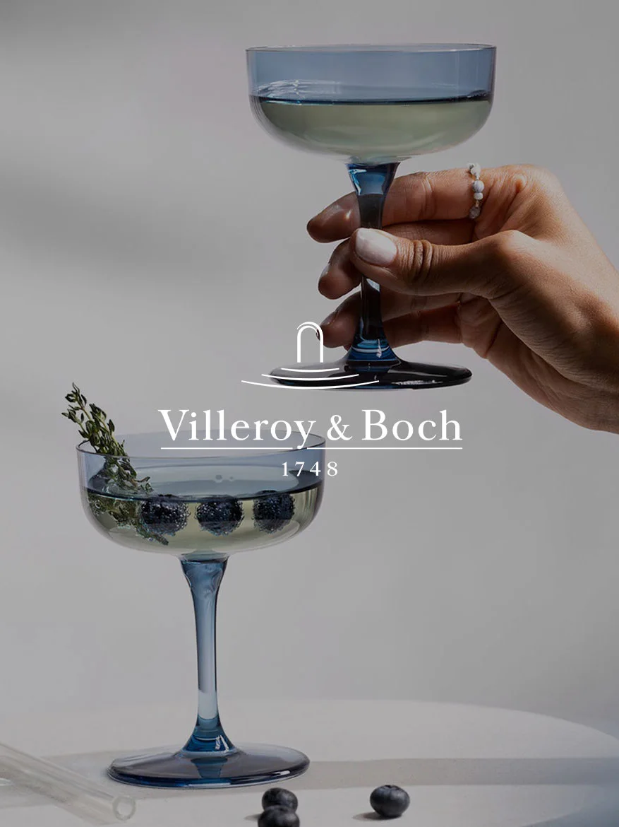 Main tient un verre coupe bleu; un autre verre en dessous avec des myrtilles, du thym et le logo Villeroy & Boch et '1748'.