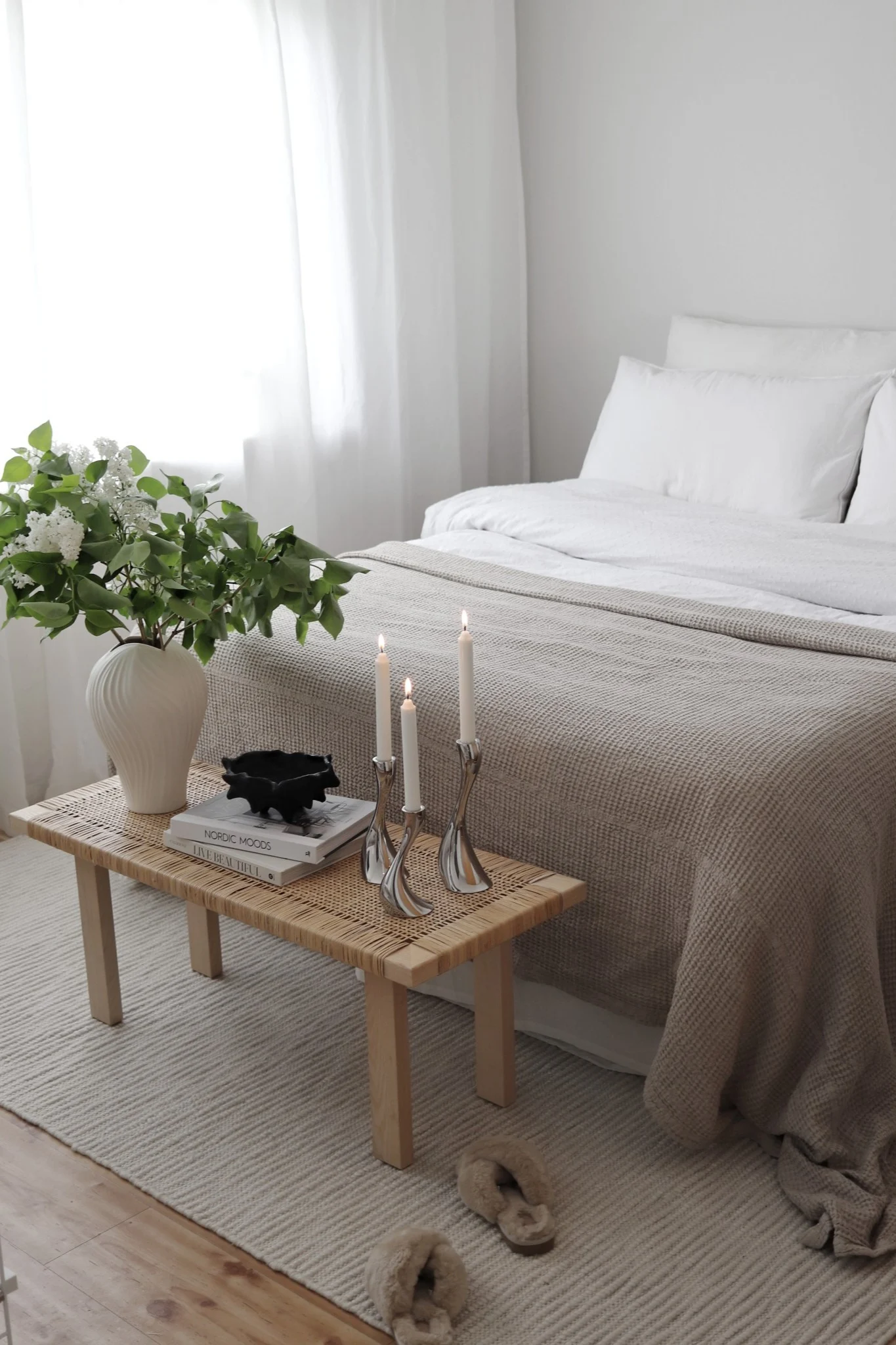 Tapis pour la chambre à coucher : le tapis blanc en laine Pebble de Scandi Living est à moitié placé sous le lit, au pied duquel se trouve un petit banc décoré d'une plante et de bougies. @hemmahosfalk