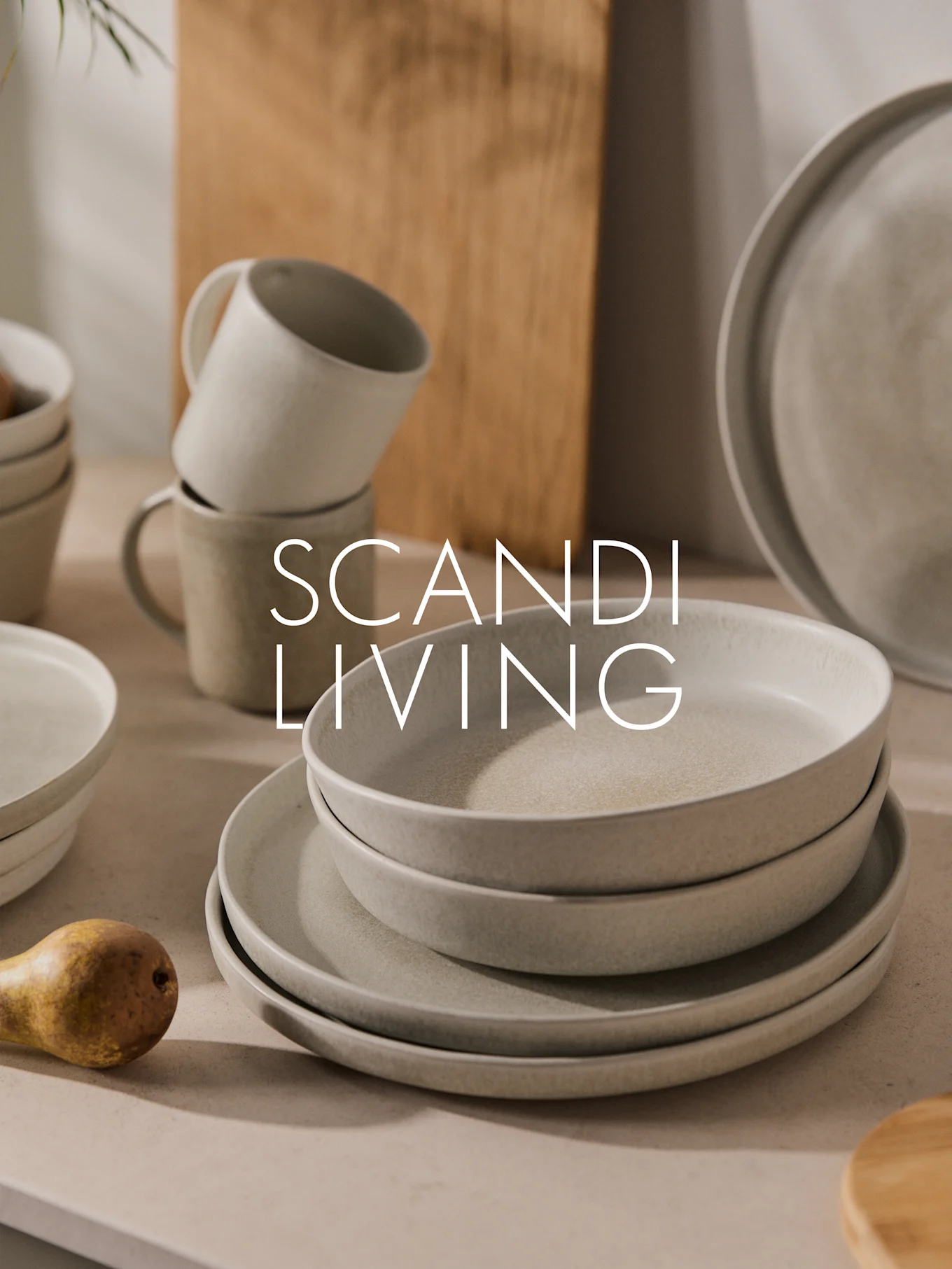 Pile d'assiettes, bols et tasses en céramique claire mouchetée avec une poire. Texte : SCANDI LIVING.