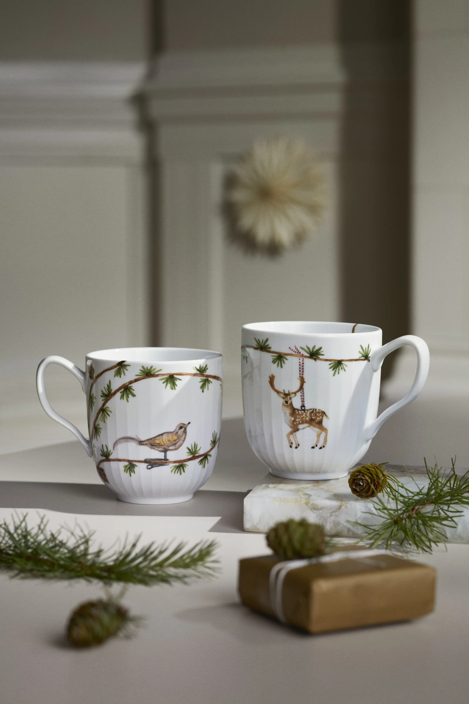 Deux tasses de Noël de la collection Hammershøi Christmas de Kähler sont posées sur une table et constituent une magnifique décoration de Noël scandinave.