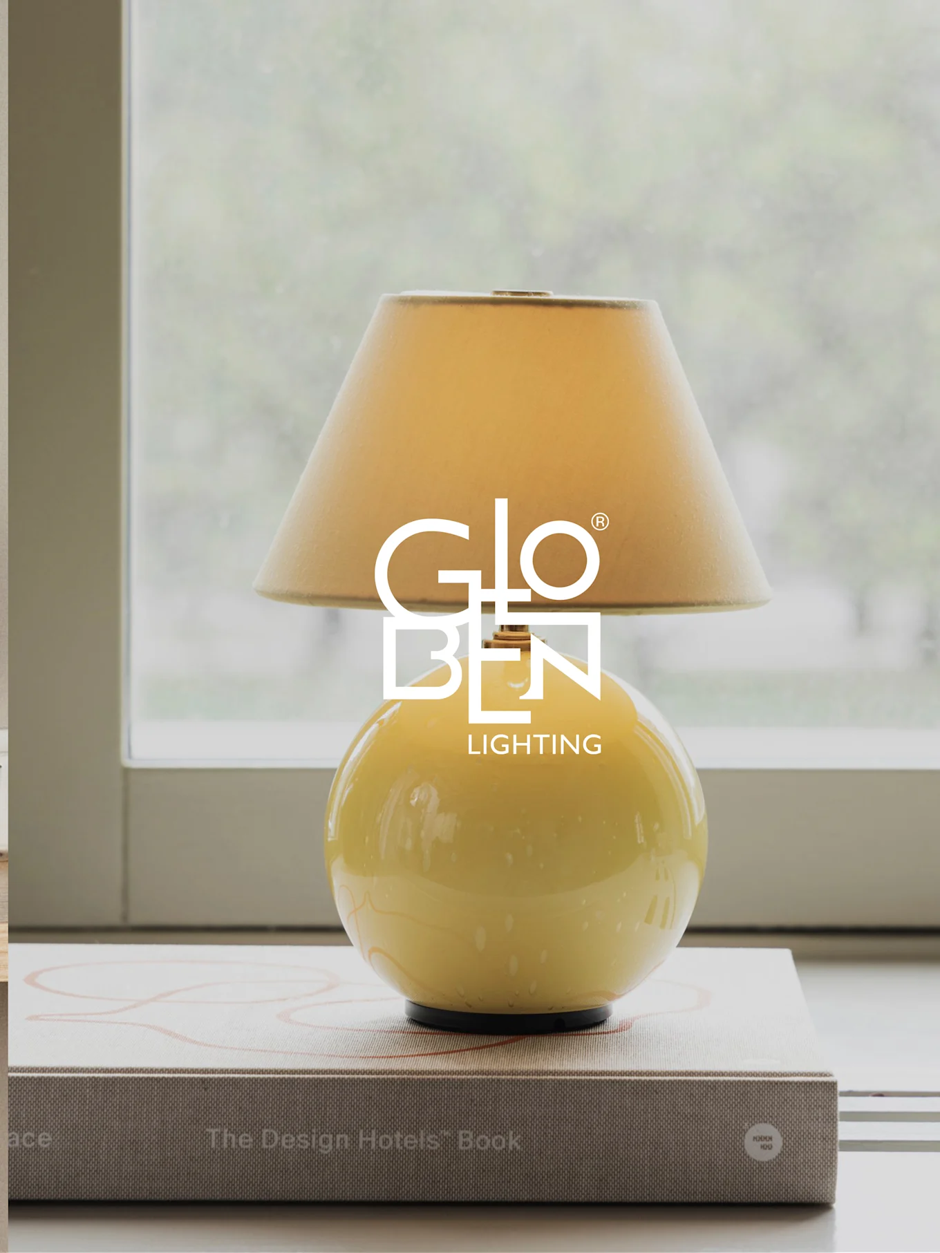 Lampe de table jaune avec abat-jour beige, posée sur des livres près d'une fenêtre.