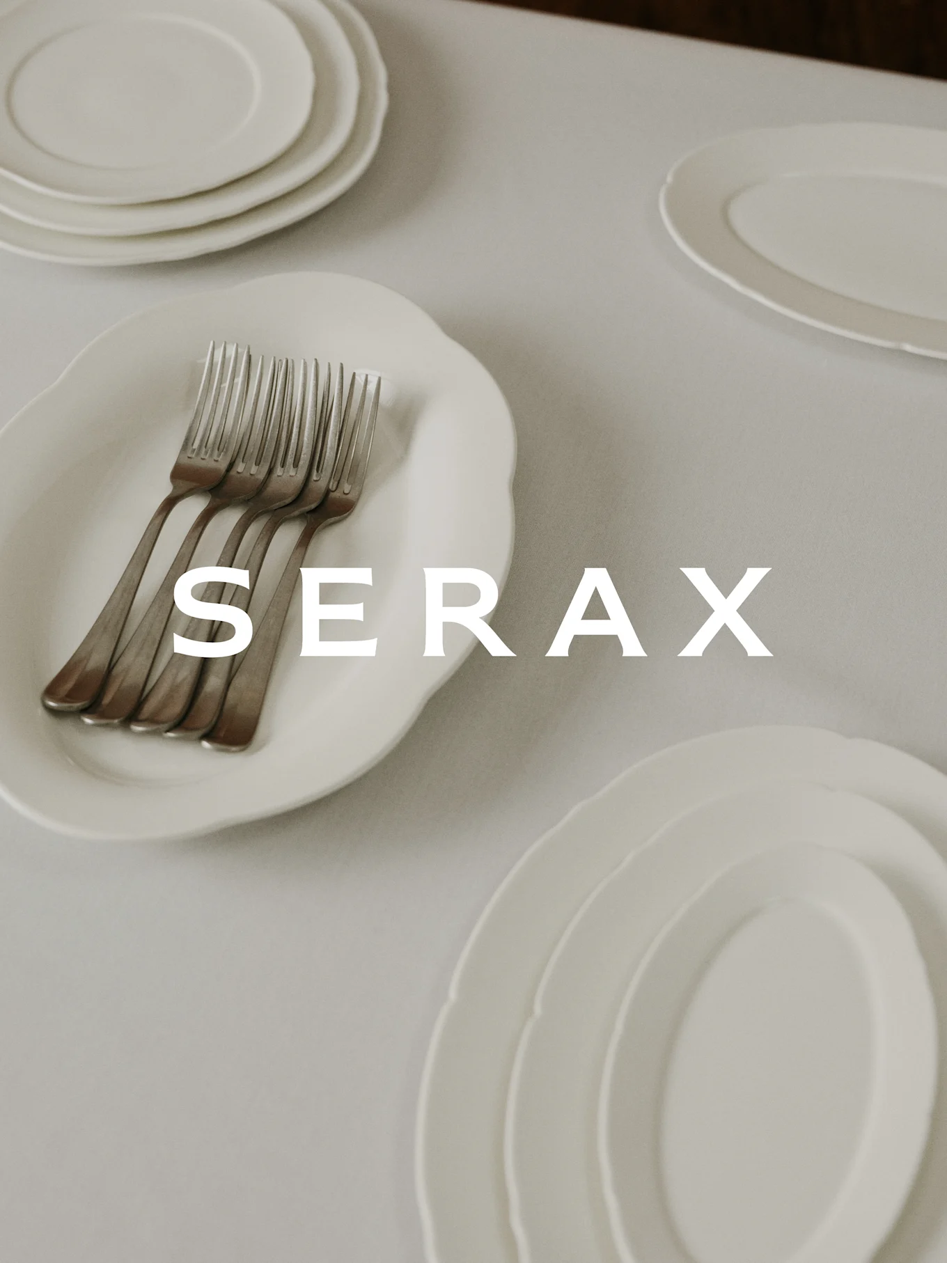 Table dressée avec des assiettes et fourchettes blanches, avec le texte 'SERAX' superposé.