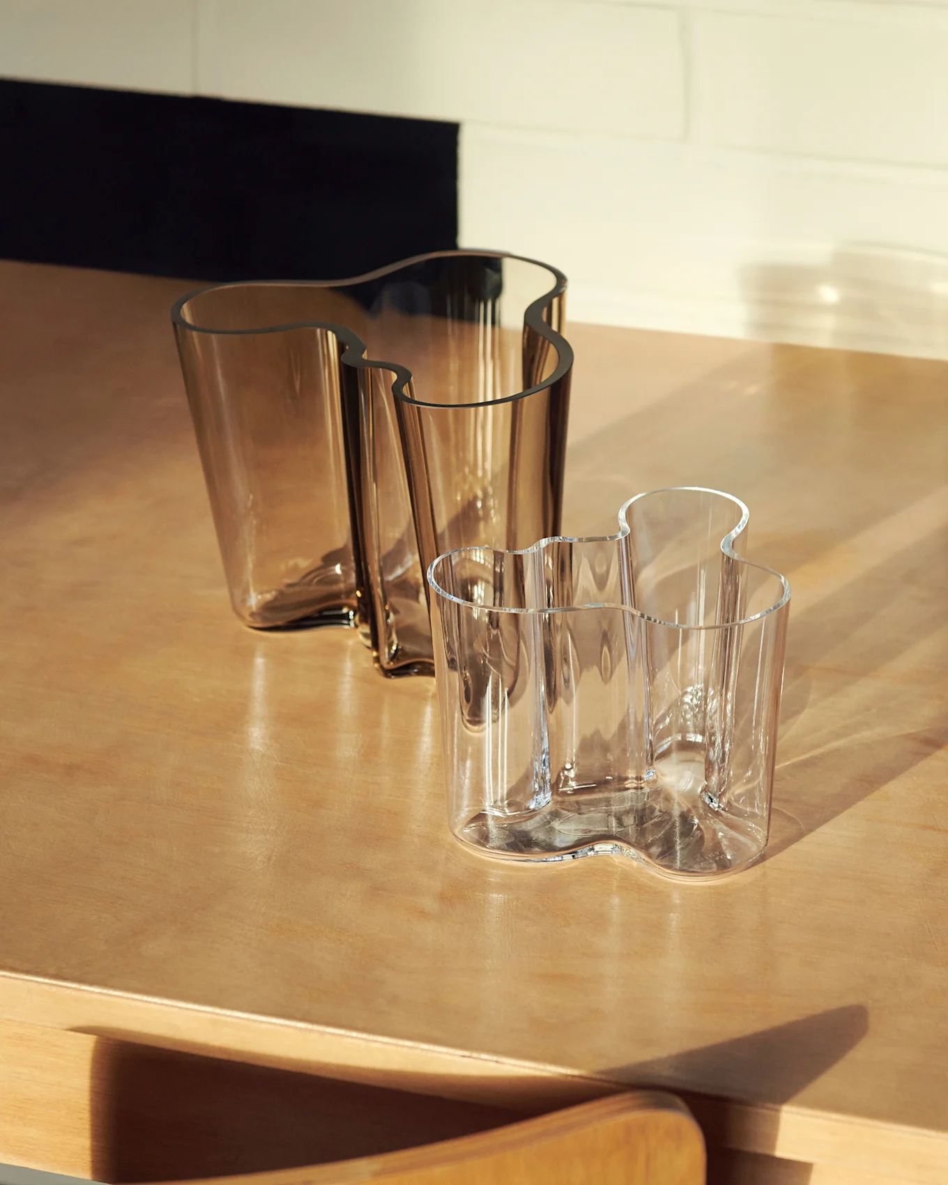 Deux vases en verre ondulés, un grand ambré et un plus petit transparent, sur une surface en bois.