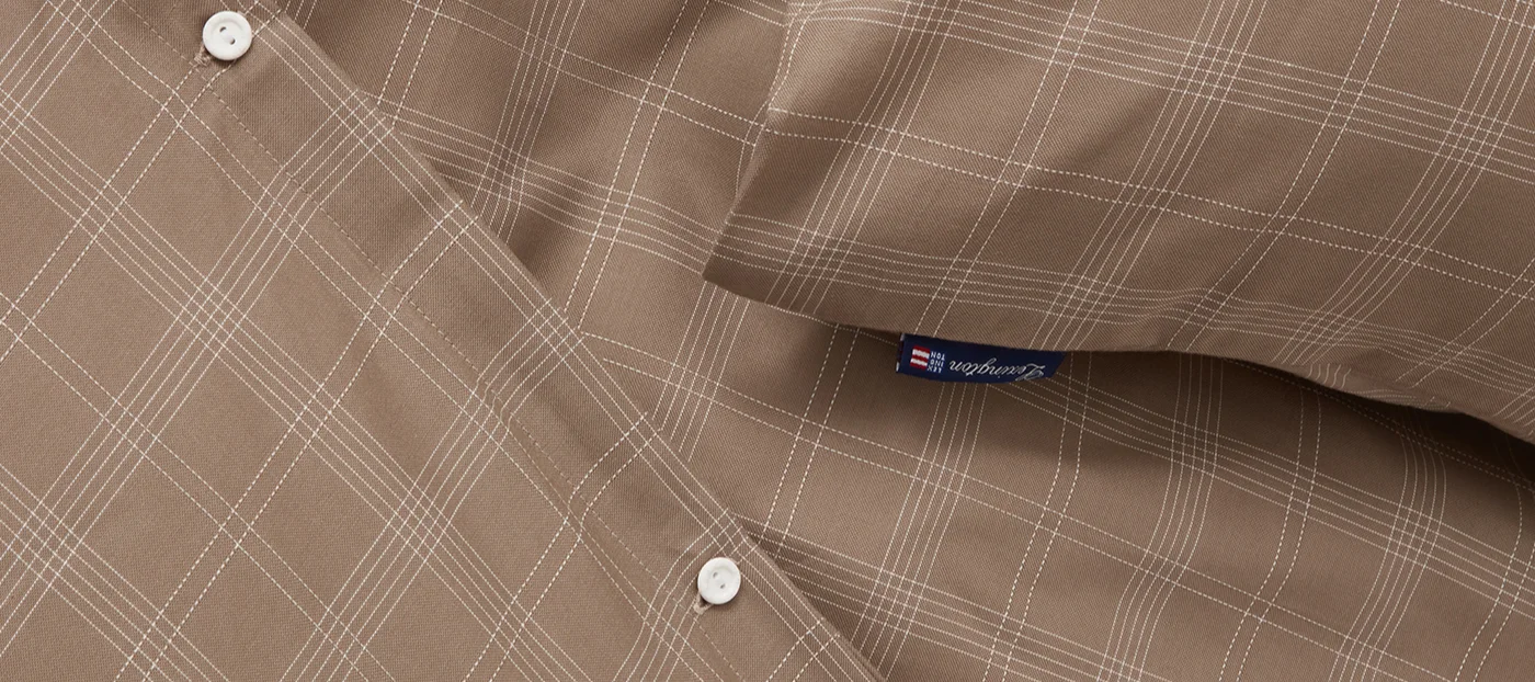 Gros plan d'un tissu marron à carreaux blancs, avec deux boutons blancs et une étiquette bleue Lexington.