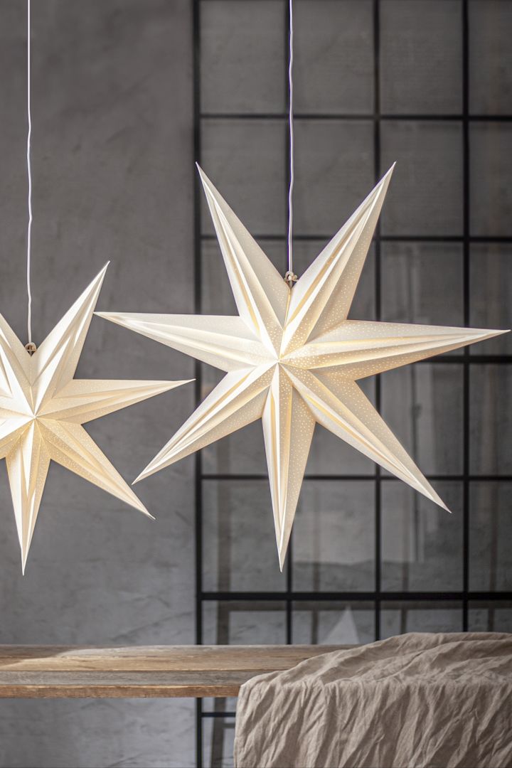 Une lanterne en papier en forme d'étoile à sept branches de Star Trading est suspendue au-dessus d'une table en bois, accompagnée d'une version plus petite. 