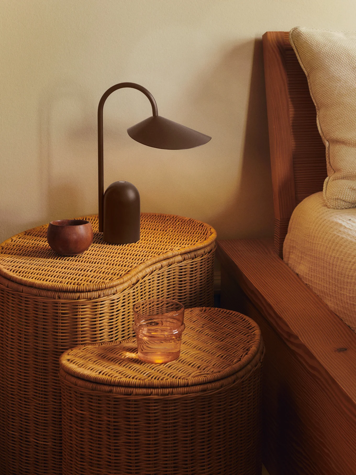Deux tables de chevet en rotin tressé avec une lampe marron foncé, un bol en bois et un verre d'eau.