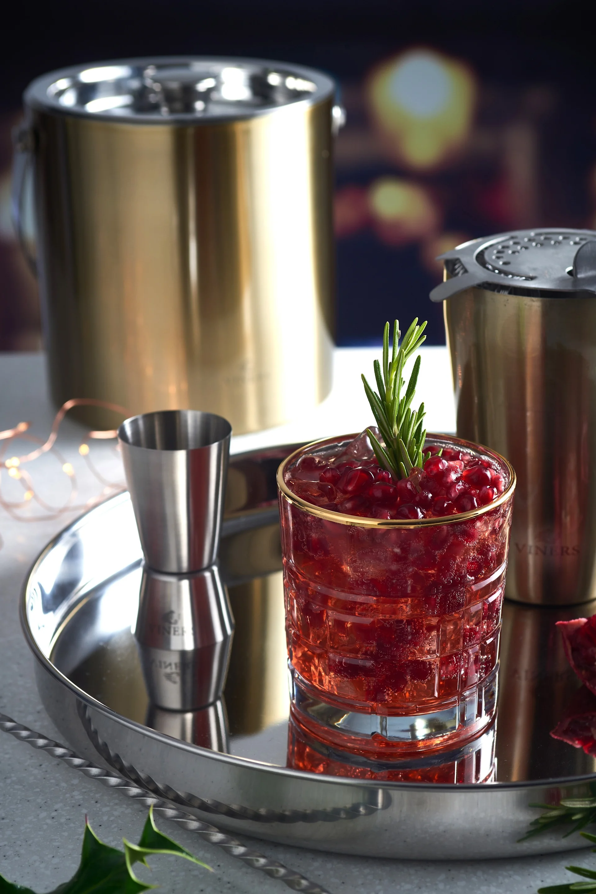 Un mocktail est posé sur un plateau en argent, à côté d'ustensiles à cocktail tels qu'un shaker et le seau à glace doré de Viners.