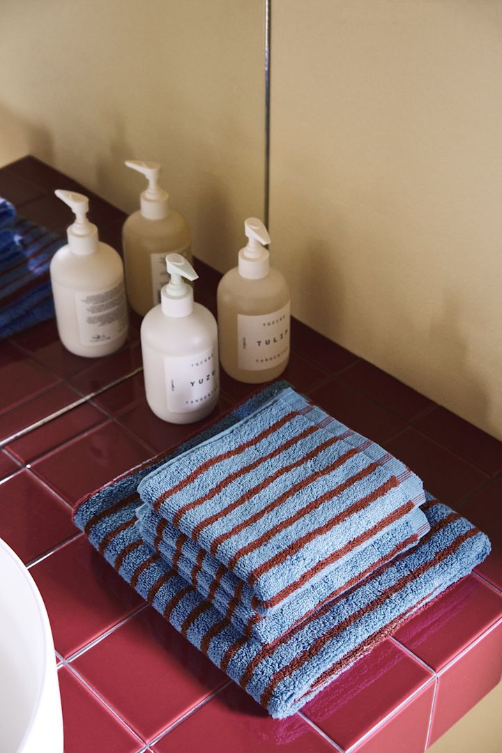 Les serviettes rayées de la collection Drift de Scandi Living sont tout à fait dans la tendance de l'automne 2025. Elles sont ici soigneusement pliées sur une étagère en carrelage rouge.