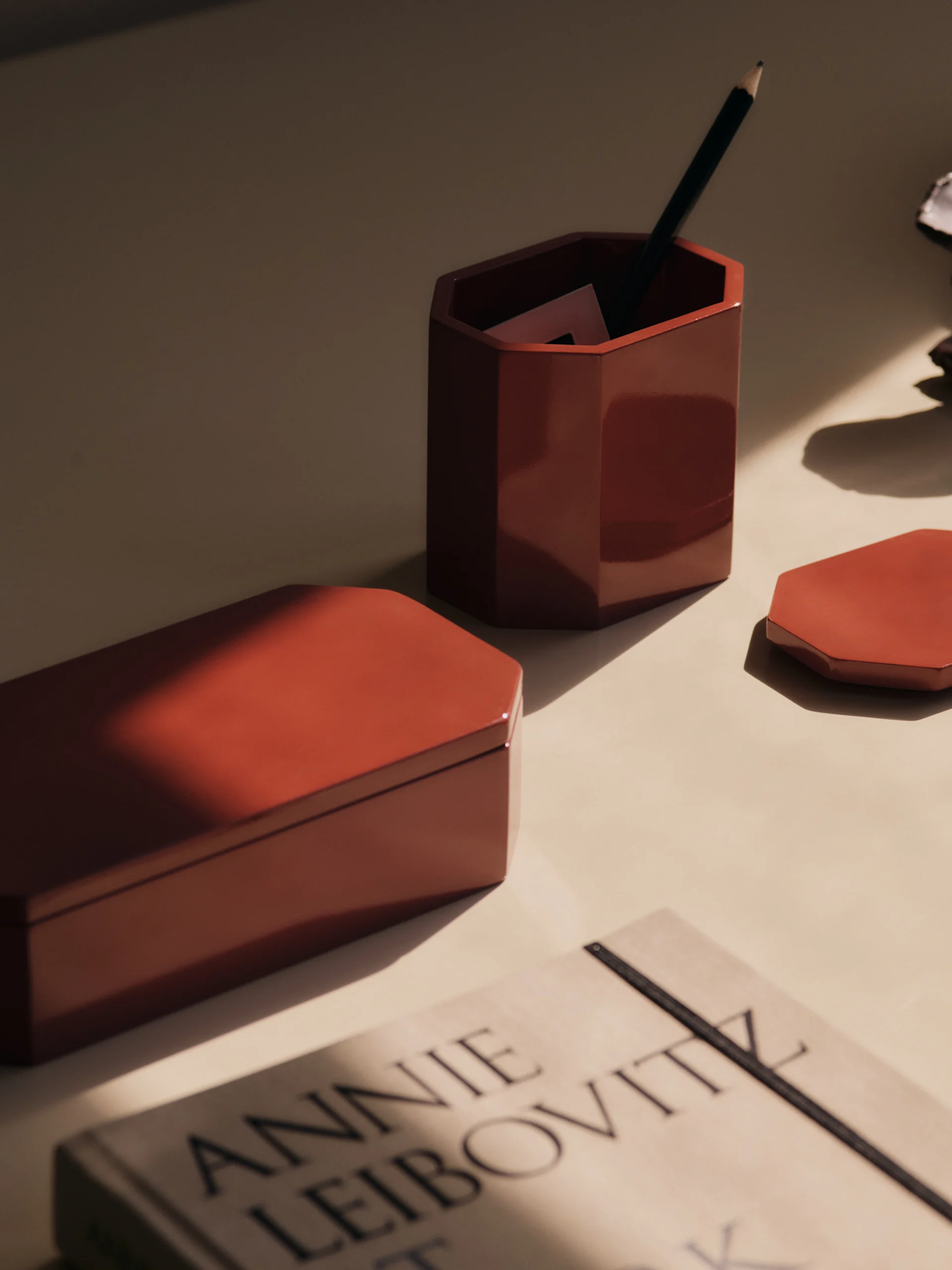 Un bureau avec des articles de rangement hexagonaux rouges, un pot à crayons et un livre, baigné de lumière solaire.