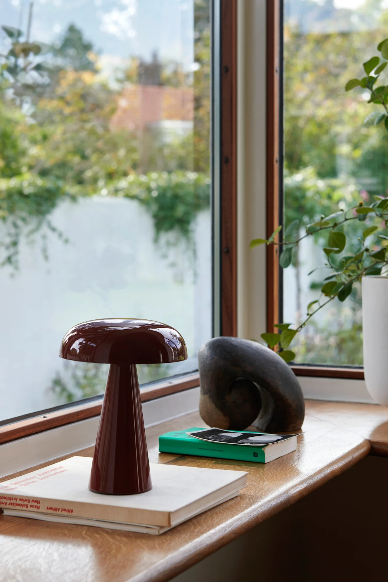 La lampe portable rouge Como de &Tradition est posée dans une fenêtre, accompagnée de livres et d'autres objets décoratifs. 