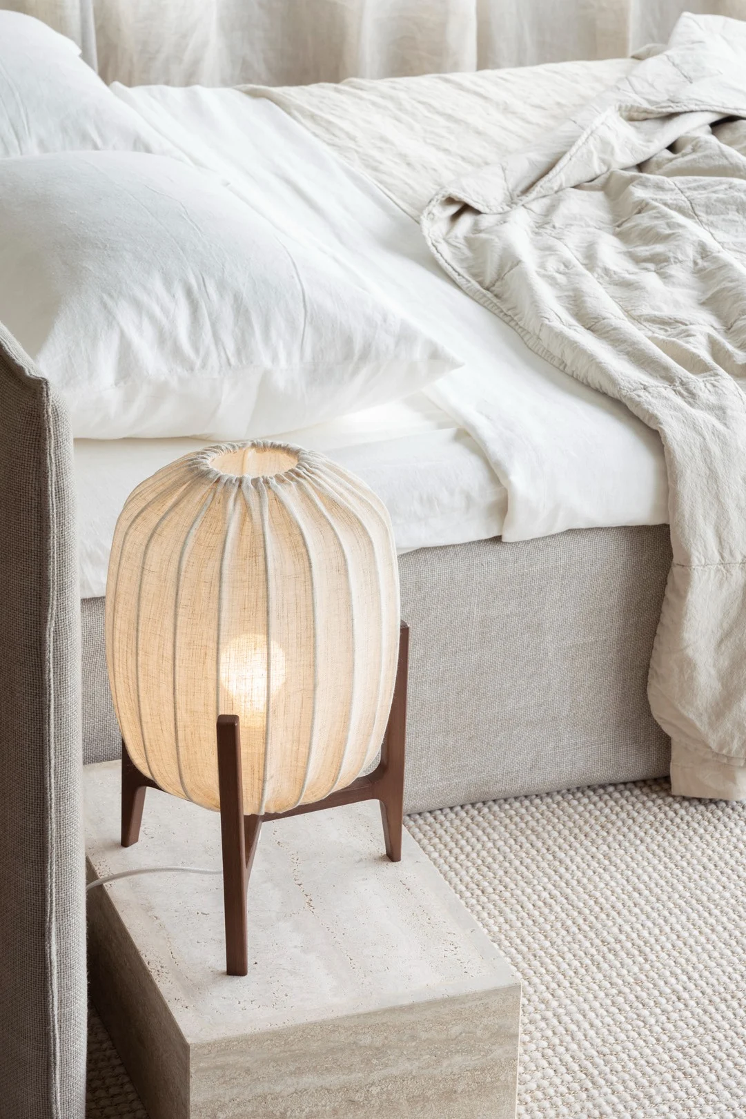 Les meubles et les accessoires en matériaux naturels comme le tissu et le bois sont parfaits pour un style d'inspiration lagom. Ici, vous voyez la lampe de table Prisma de Watt & Veke posée à côté d'un lit.